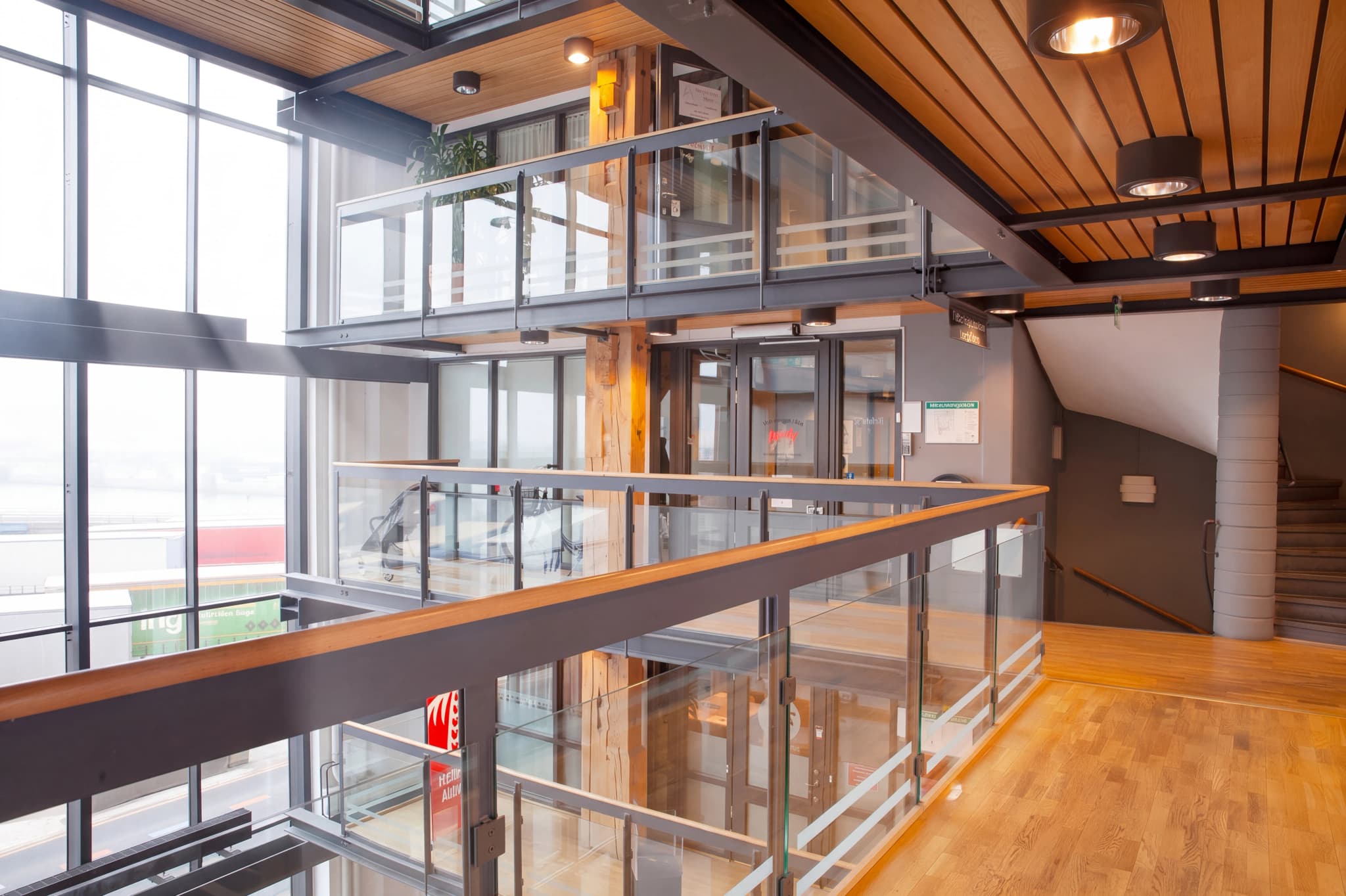 Interiör av en modern kontorsbyggnad med en glasbalkong och stora fönster som visar en utsikt över hamnen.