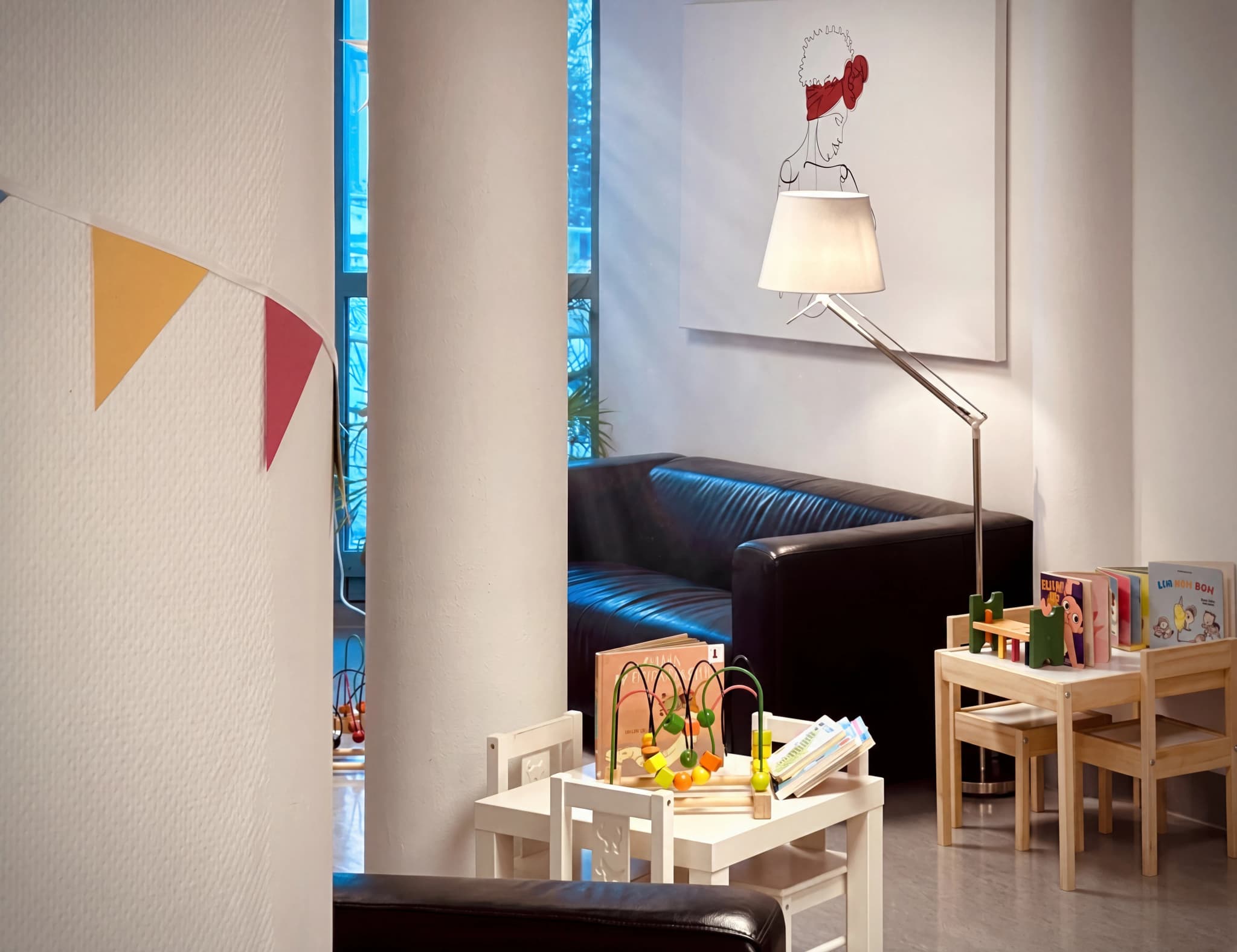 Ett barnvänligt väntrum med små möbler, leksaker, böcker och en soffa.