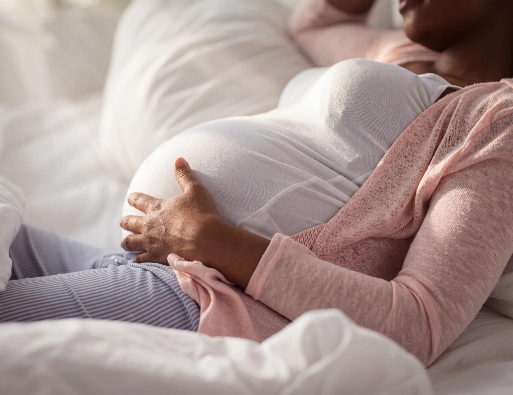 Gravid kvinna som håller sin mage medan hon ligger i en säng med mjuka täcken.