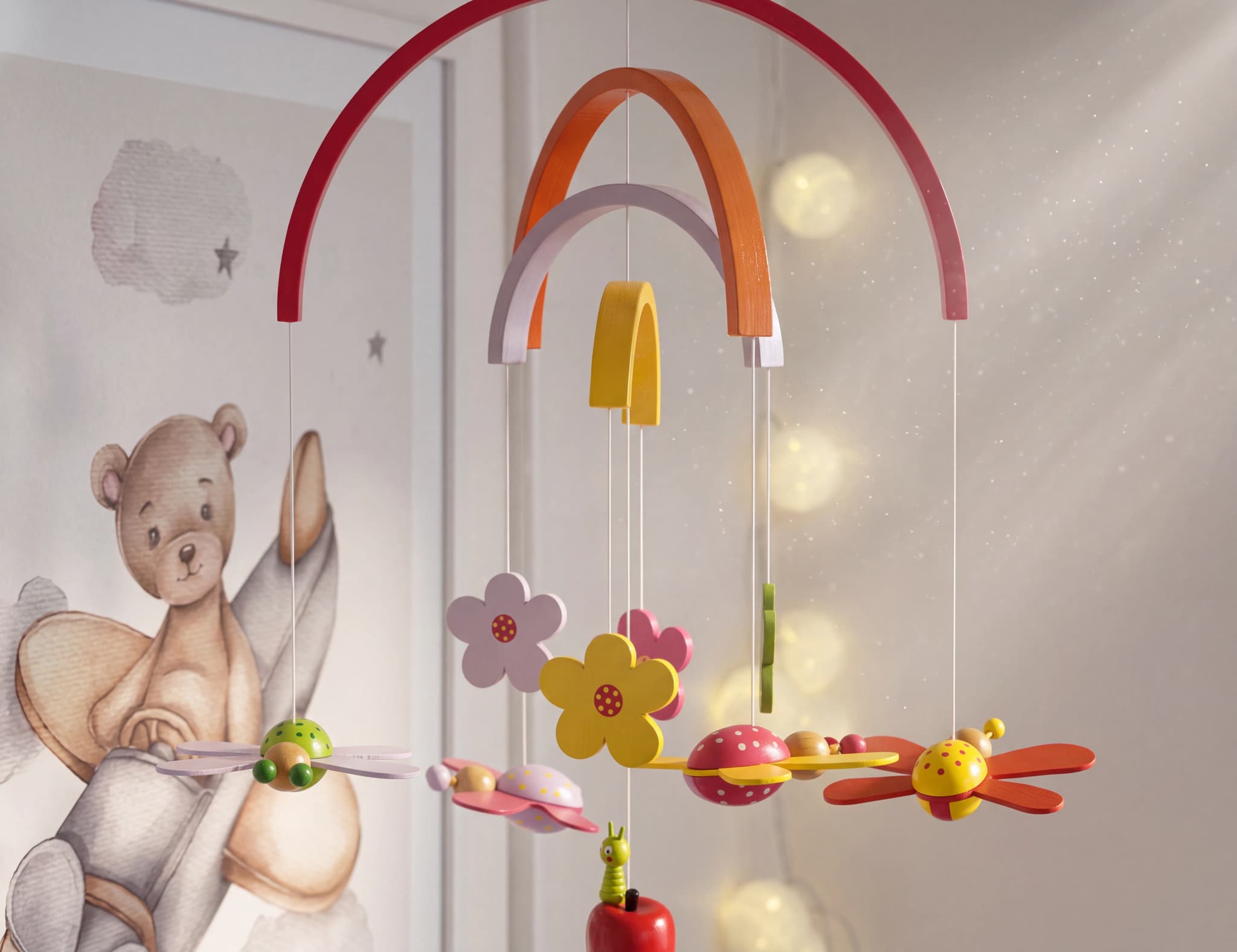 En babymobil med färgglada träleksaker i form av djur och blommor, hängande över en barnsäng.