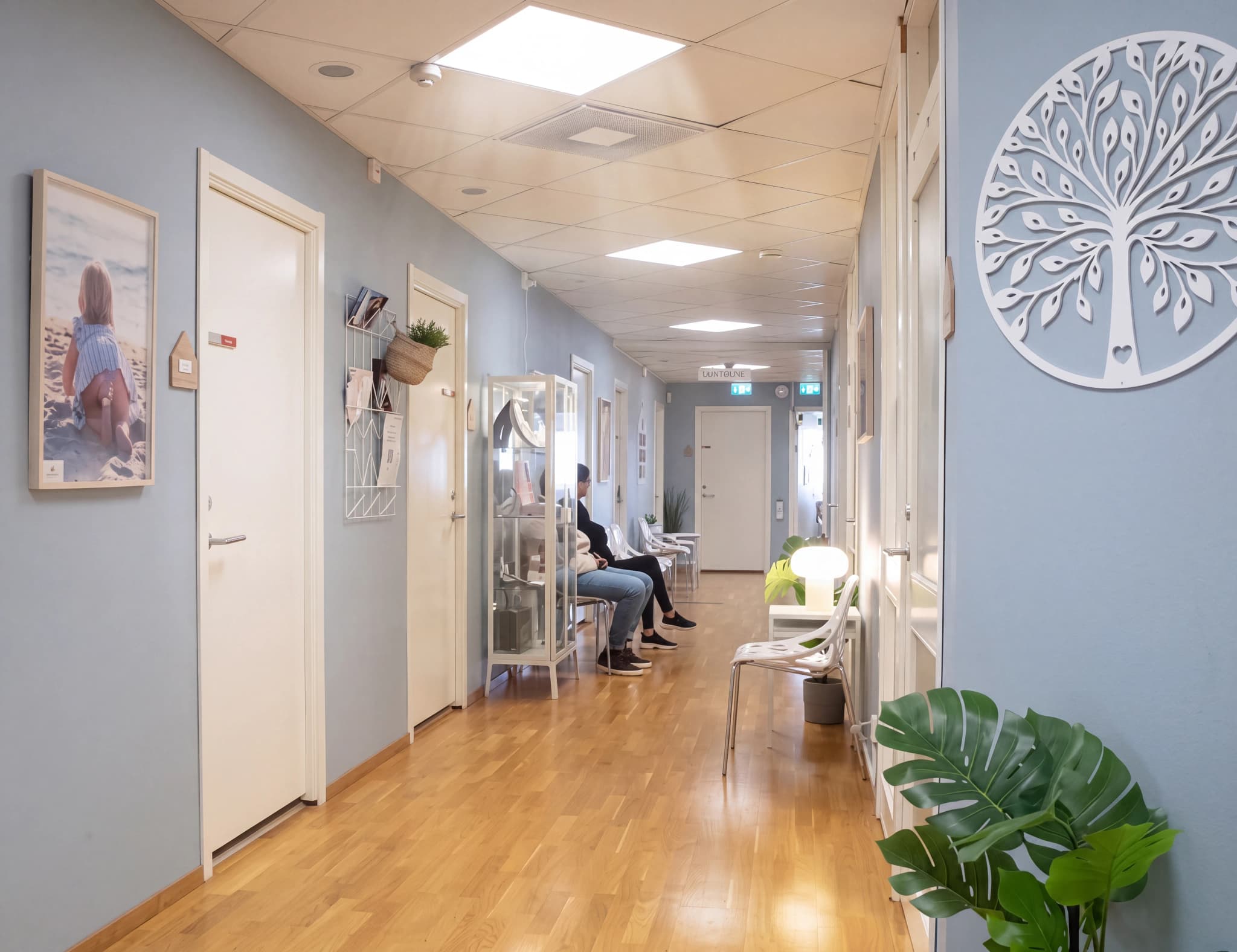 Väntrumskorridor på en klinik med väntande patienter och konst på väggarna.