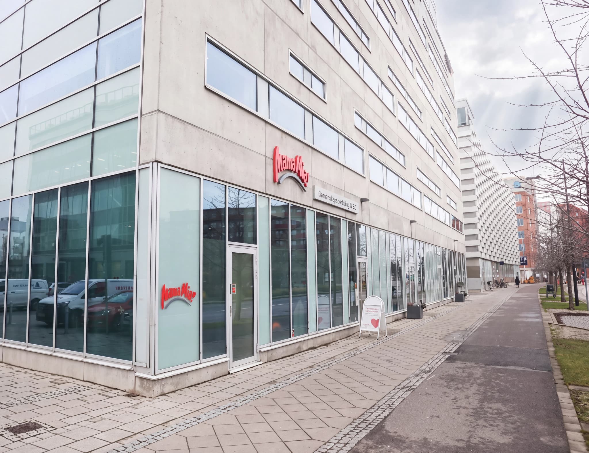 Yttre av en modern byggnad med glasfasad där en medicinsk klinik, Mama Mia, har sin skyltning.