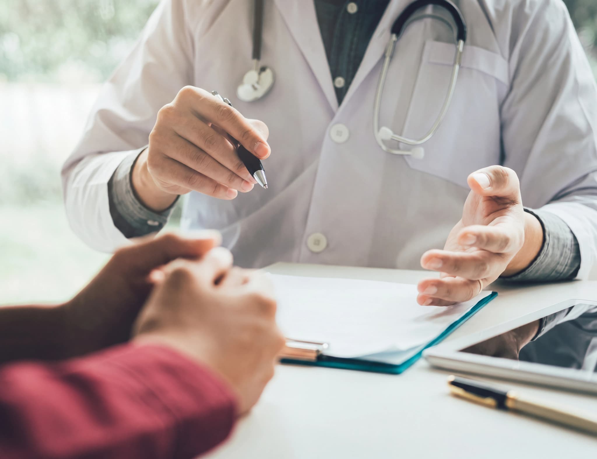Läkare i vit rock förklarar ett dokument för en patient, med en penna i handen.