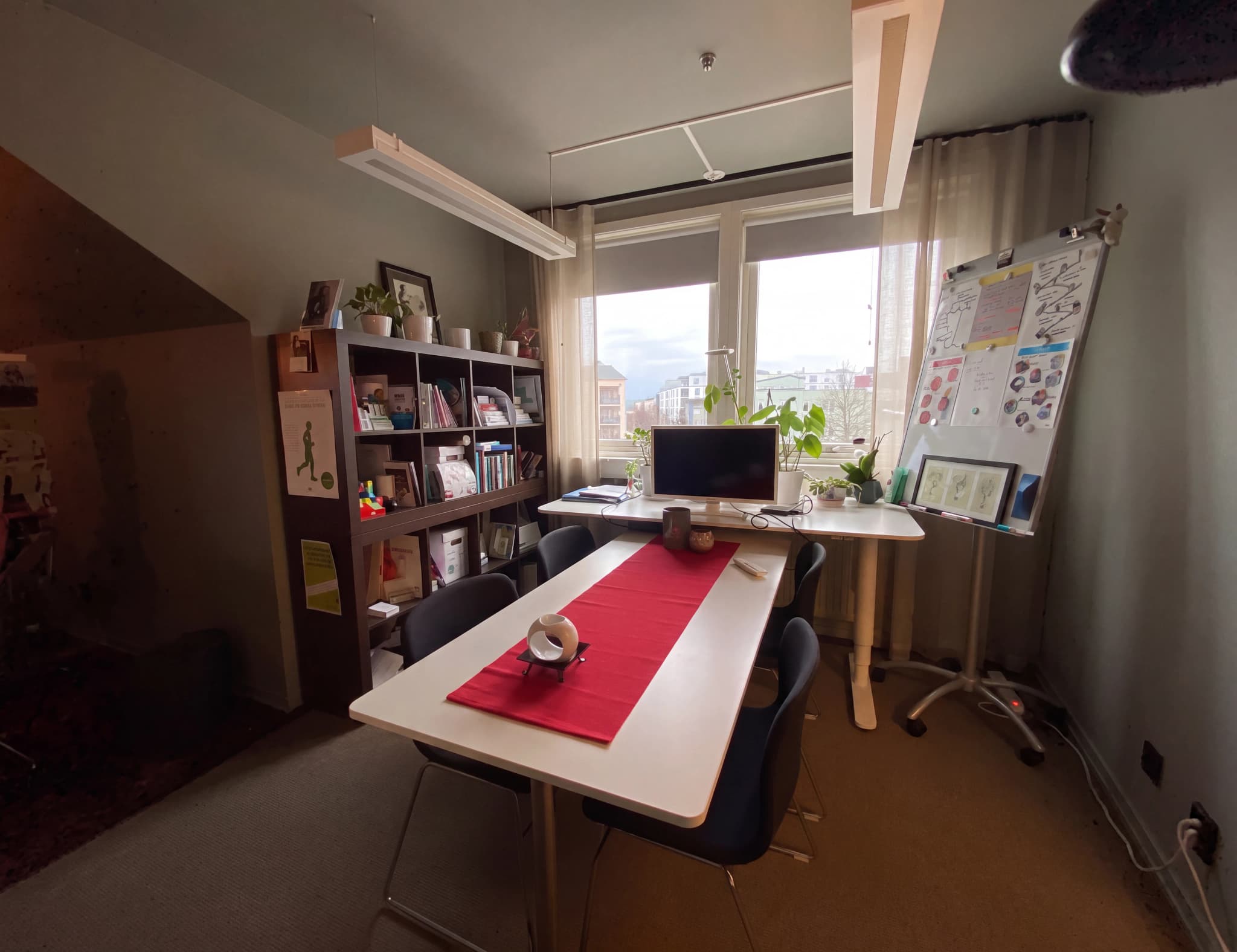 Ett modernt kontorsutrymme med ett höj- och sänkbart skrivbord, en datorskärm och en whiteboardtavla vid ett fönster.