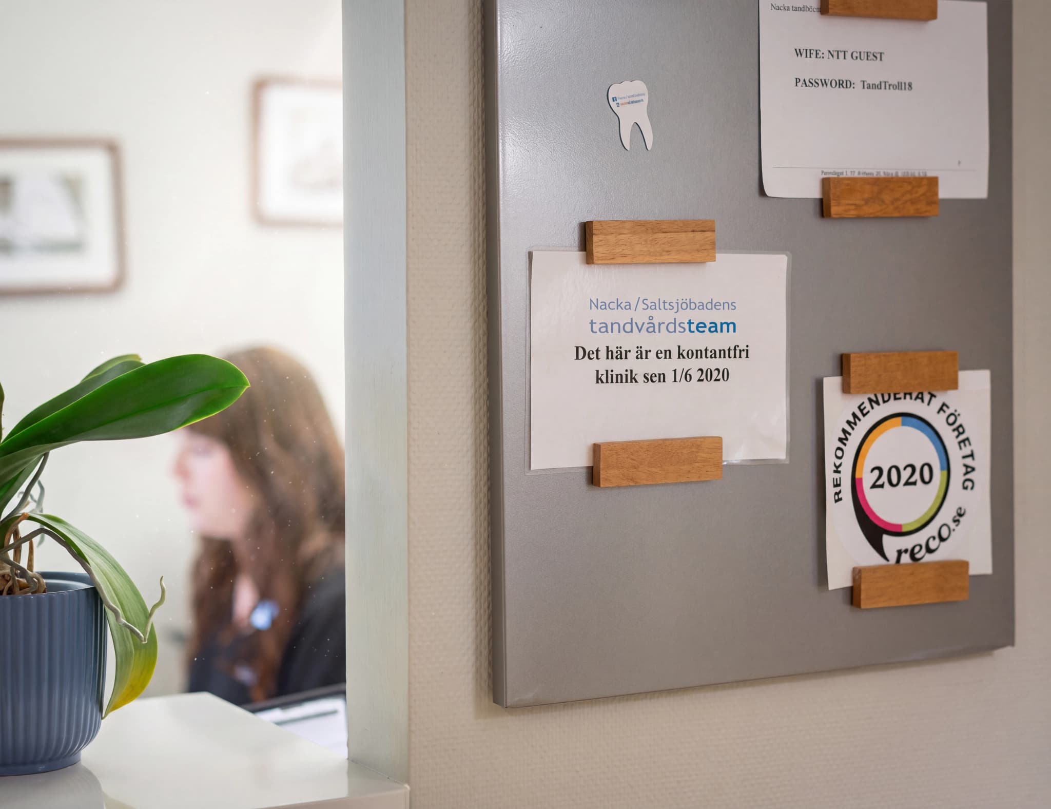 En kylskåpsdörr med flera lappar fästa med träklämmor, inklusive information om en tandvårdsklinik och en rekommendationslogotyp.