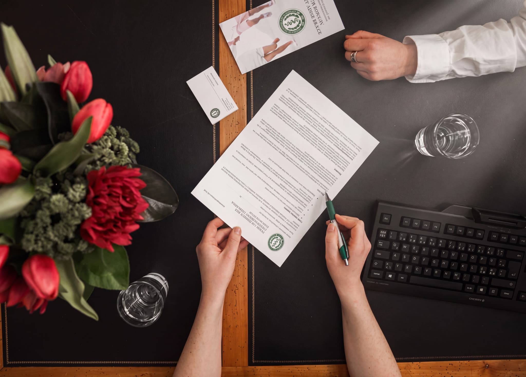 Två personers händer på ett skrivbord, en signerade ett dokument med en penna och den andra har en ring på fingret.