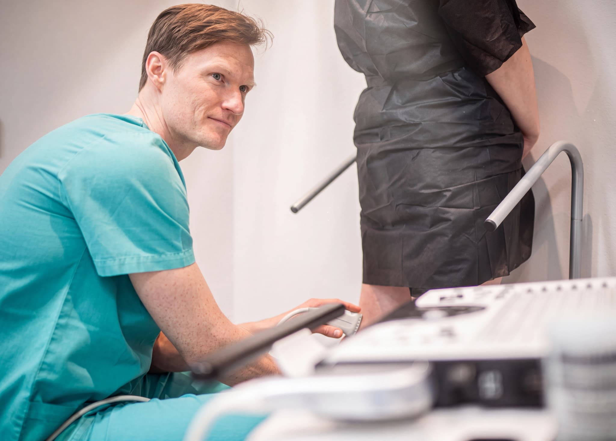 Läkare i grön uniform som utför en ultraljudsundersökning på en patients ben.