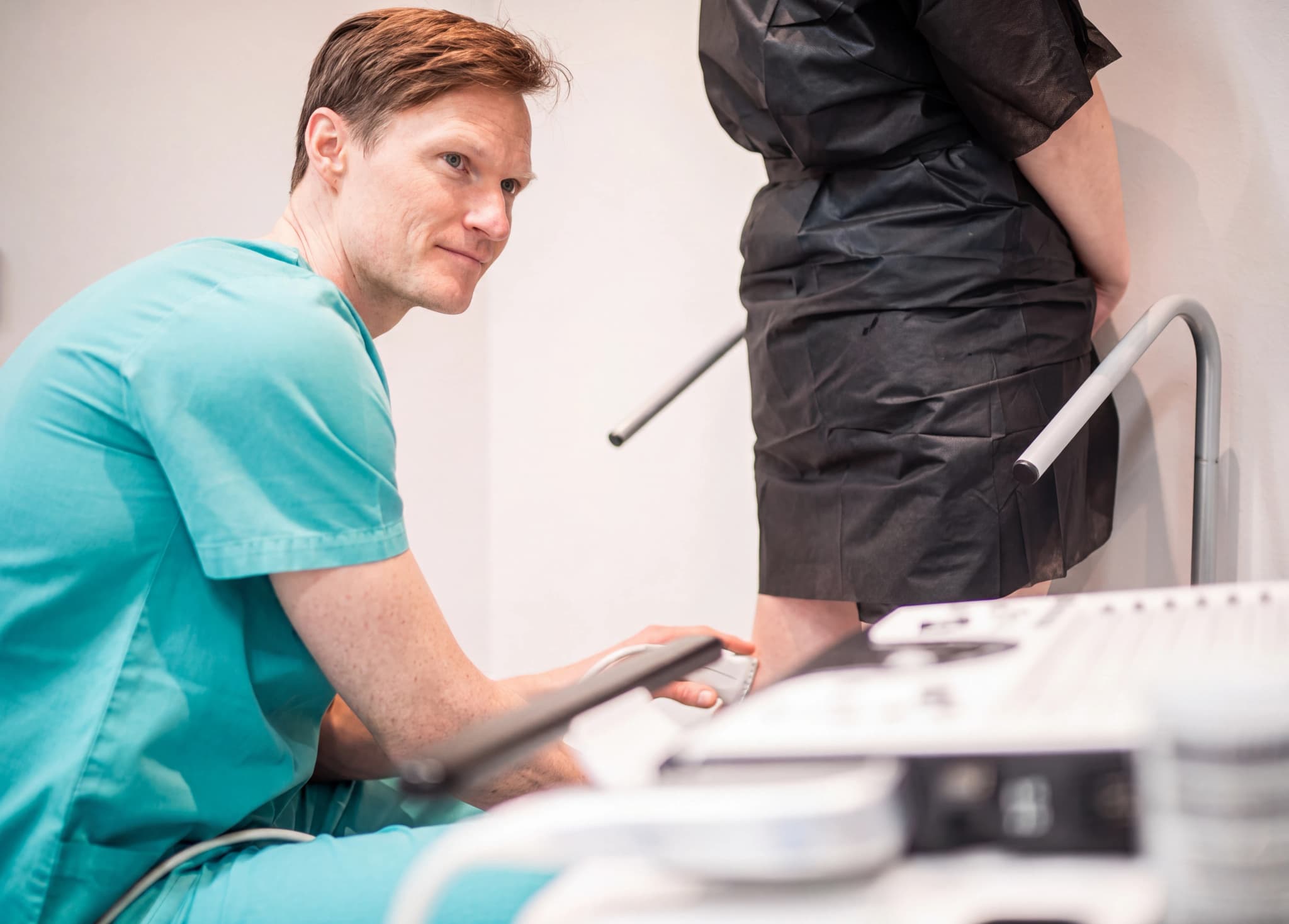 Läkare i gröna kläder använder ultraljudsapparat på en patients ben