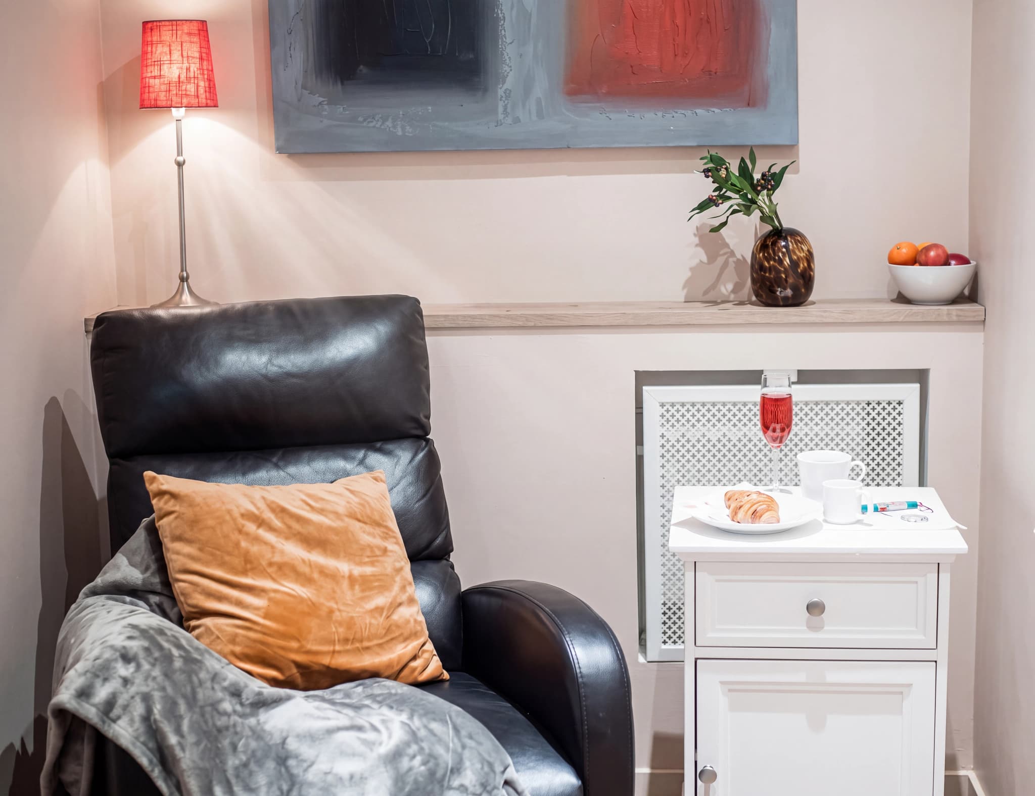 En svart läderfåtölj med en orange kudde och en grå filt ligger i ett rum med en golvlampa och en liten sidobord.