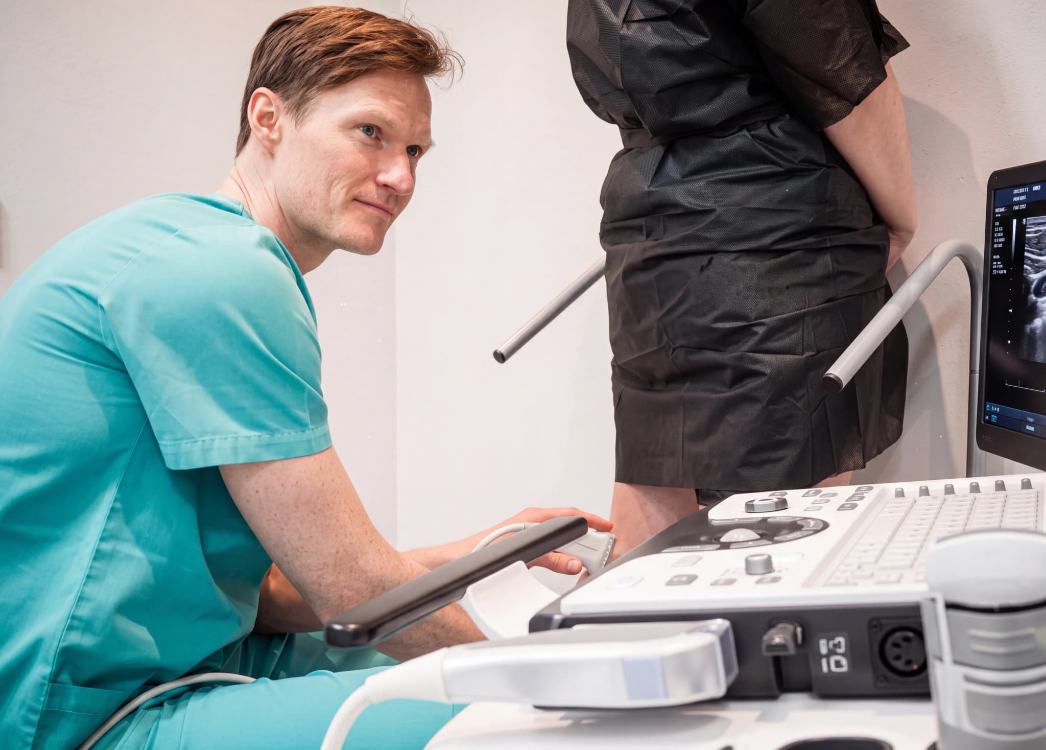 Läkare i grön skrubb använder ultraljudsapparat på en patients ben