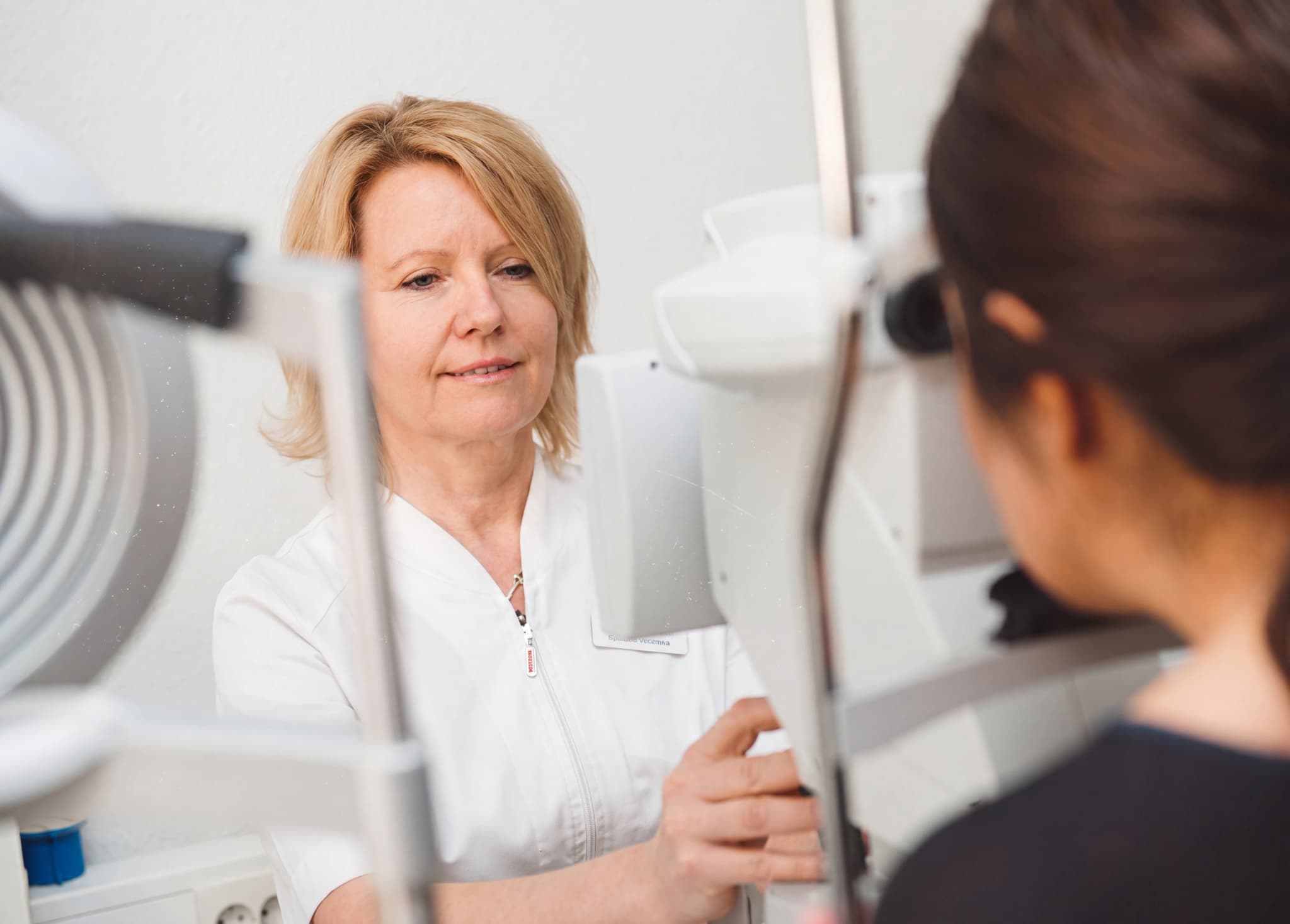Optiker som undersöker patientens ögon med en undersökningsutrustning i en klinik.