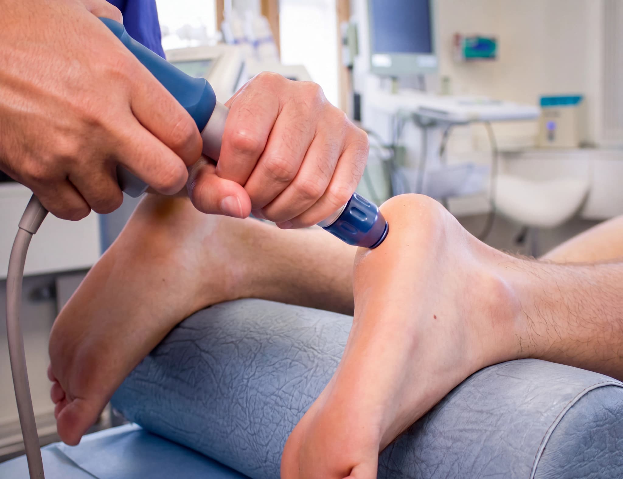 Fysioterapeut använder stötvågsbehandling på en patients häl.