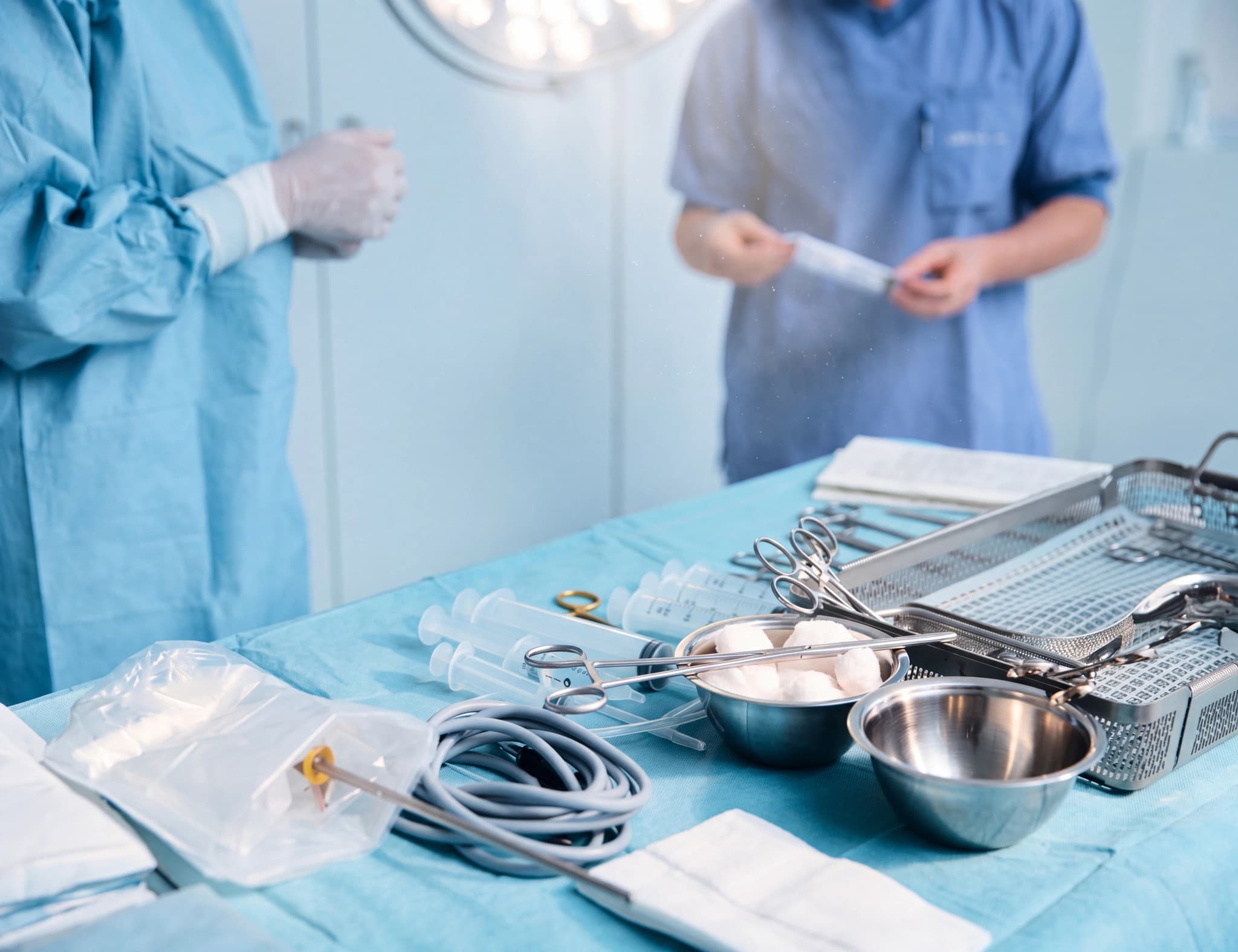 Kirurgiska instrument redo på ett bord i en operationssal, med vårdpersonal i bakgrunden.