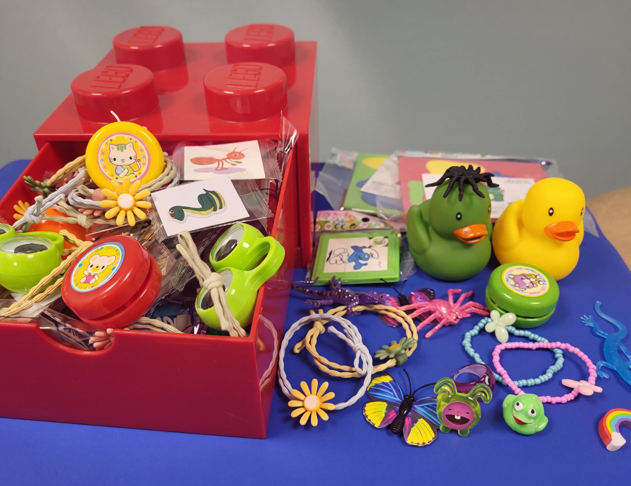 Röd leksakslåda i legostil fylld med olika små leksaker som yo-yos, hopprep, figurer och gummiankor.