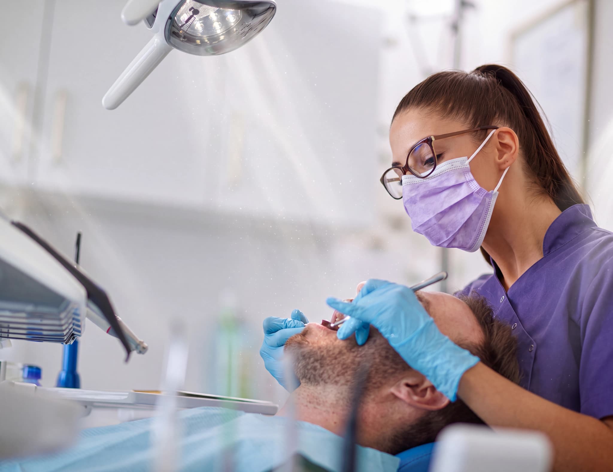 Tandläkare i skyddsutrustning undersöker en patients tänder med instrument i en tandläkarmottagning.