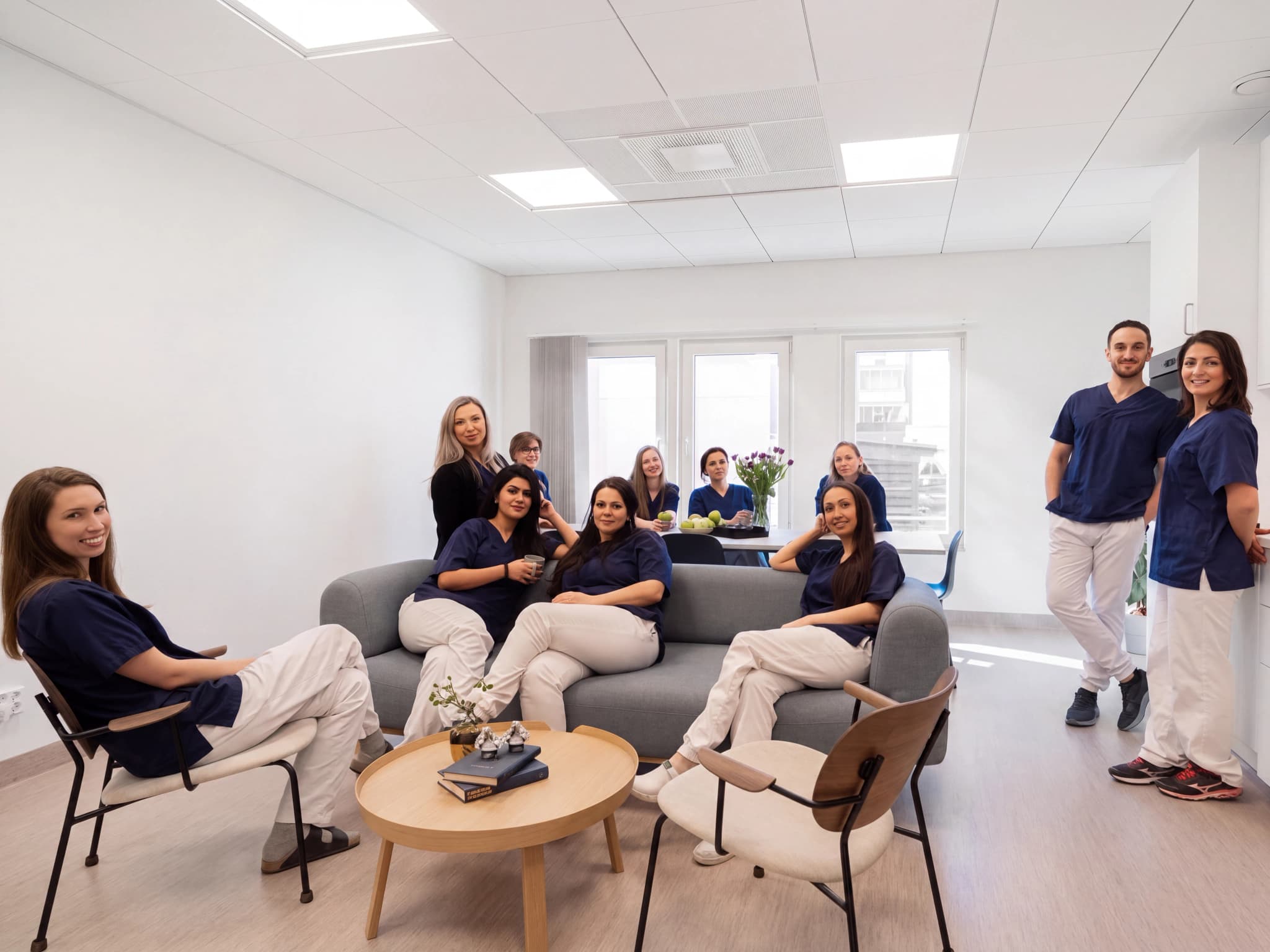 Ett team av hälso- och sjukvårdspersonal vilar och pratar i ett modernt loungeområde, klädda i scrubs.