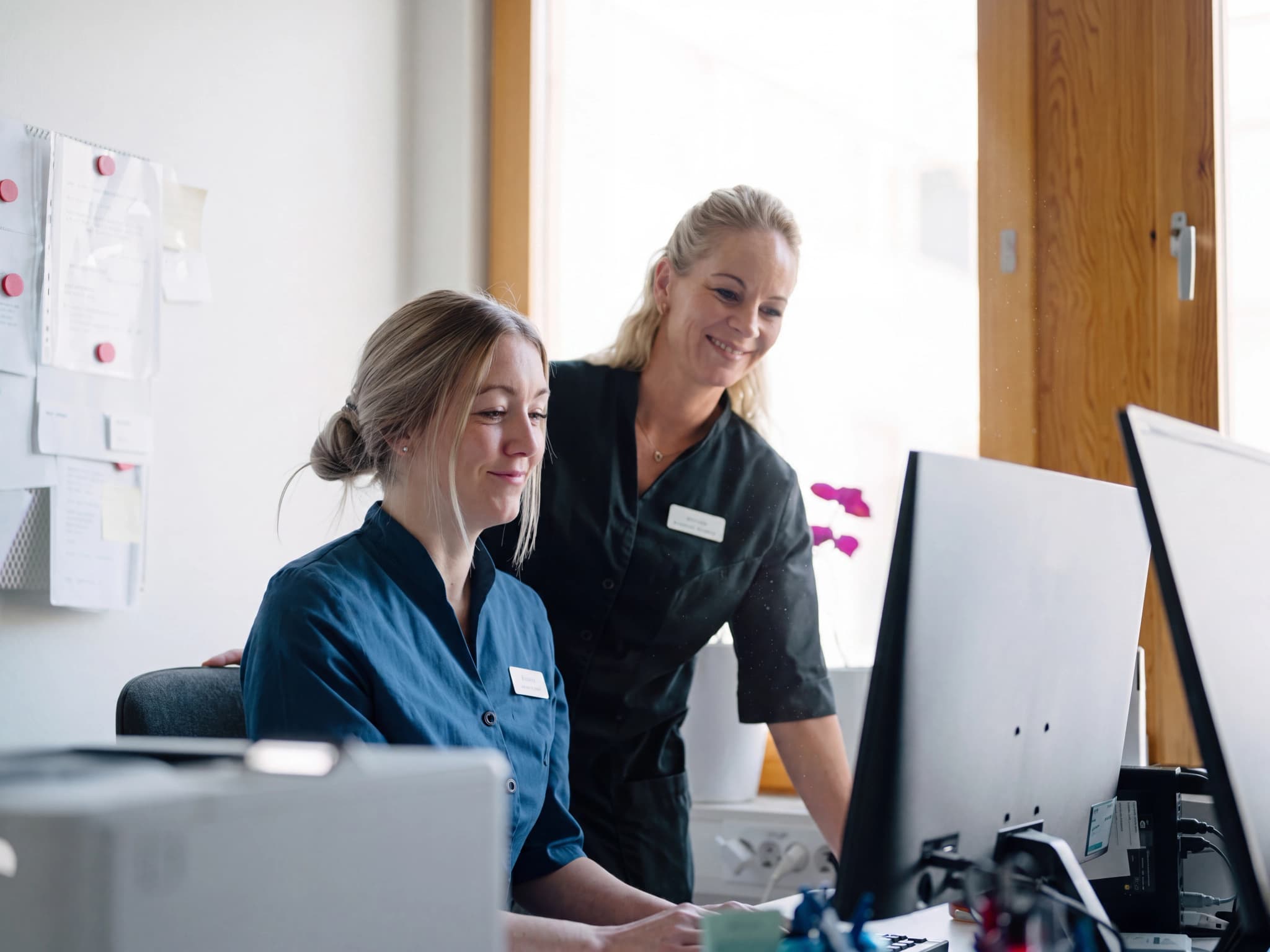 Två kvinnor som arbetar vid ett receptionbordsdator.