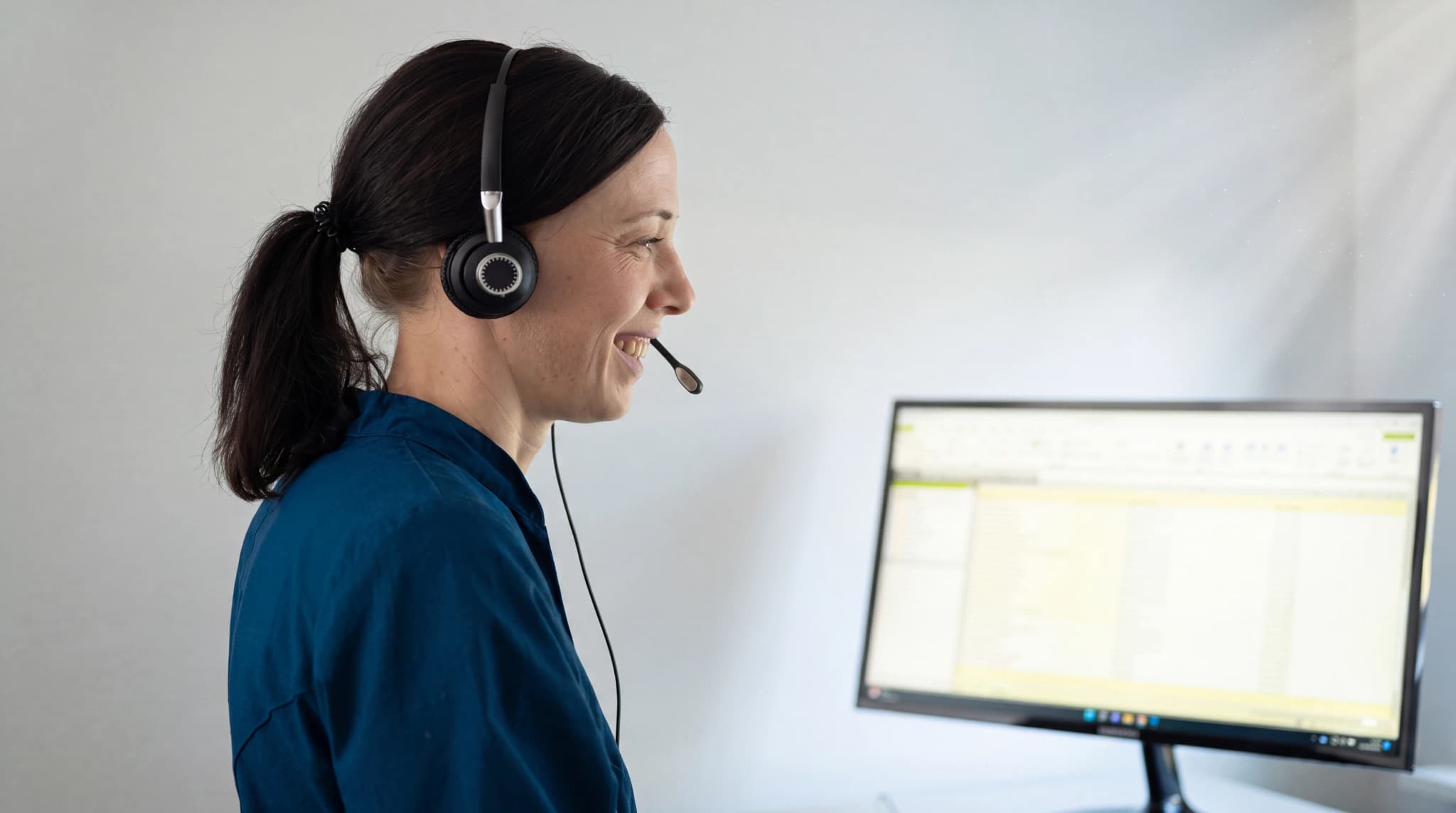 En kvinna med headset och mikrofon talar medan hon sitter vid en dator på ett kontor.