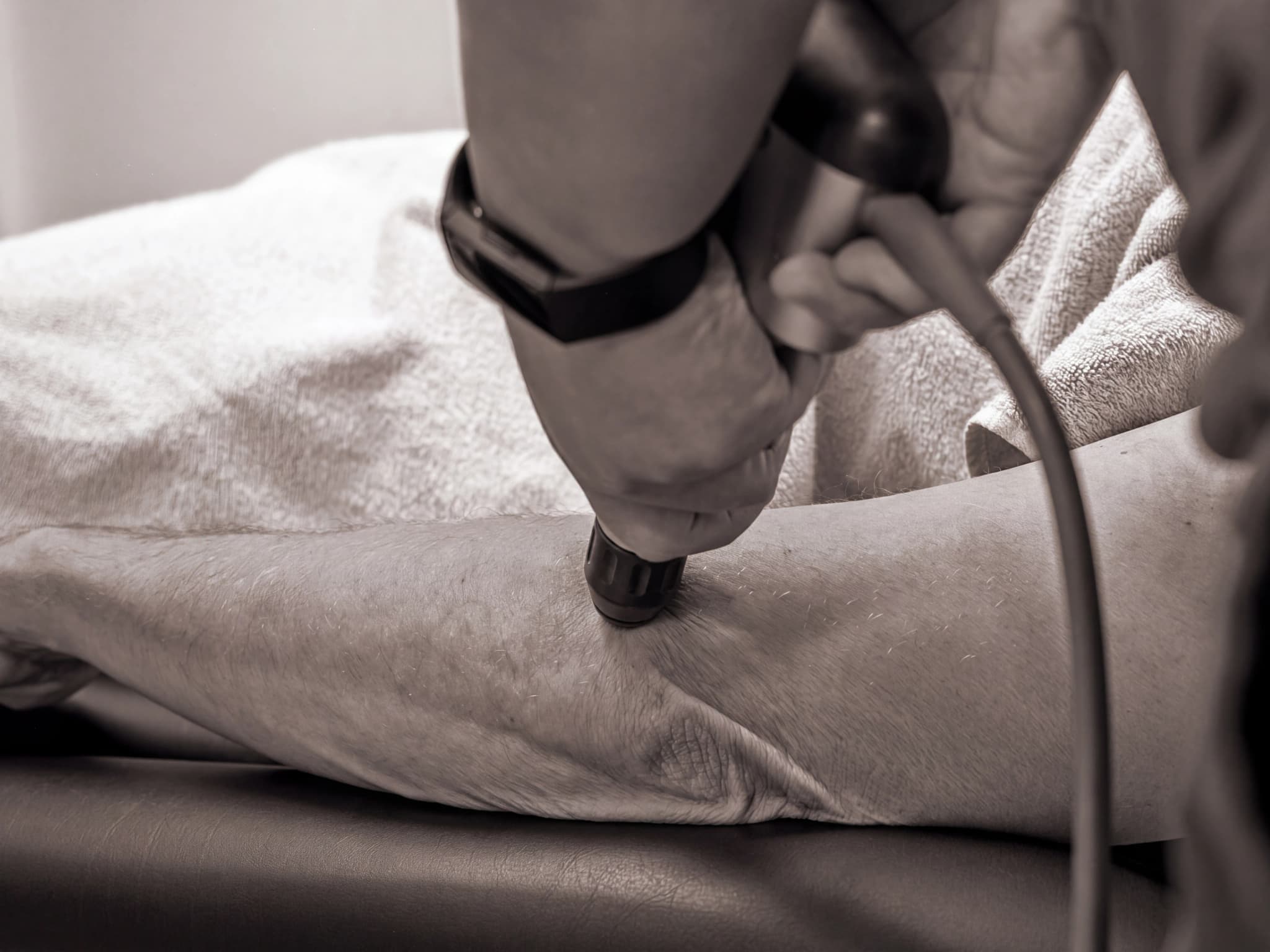 Fysioterapeut använder ultraljudsapparat på en patients ben.