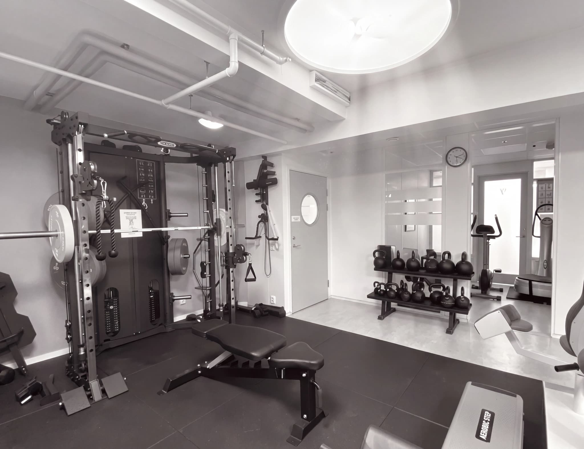 Ett modernt gym med styrketräningsutrustning som smith machine, bänkar, hantlar och vikter, beläget i ett ljust rum.