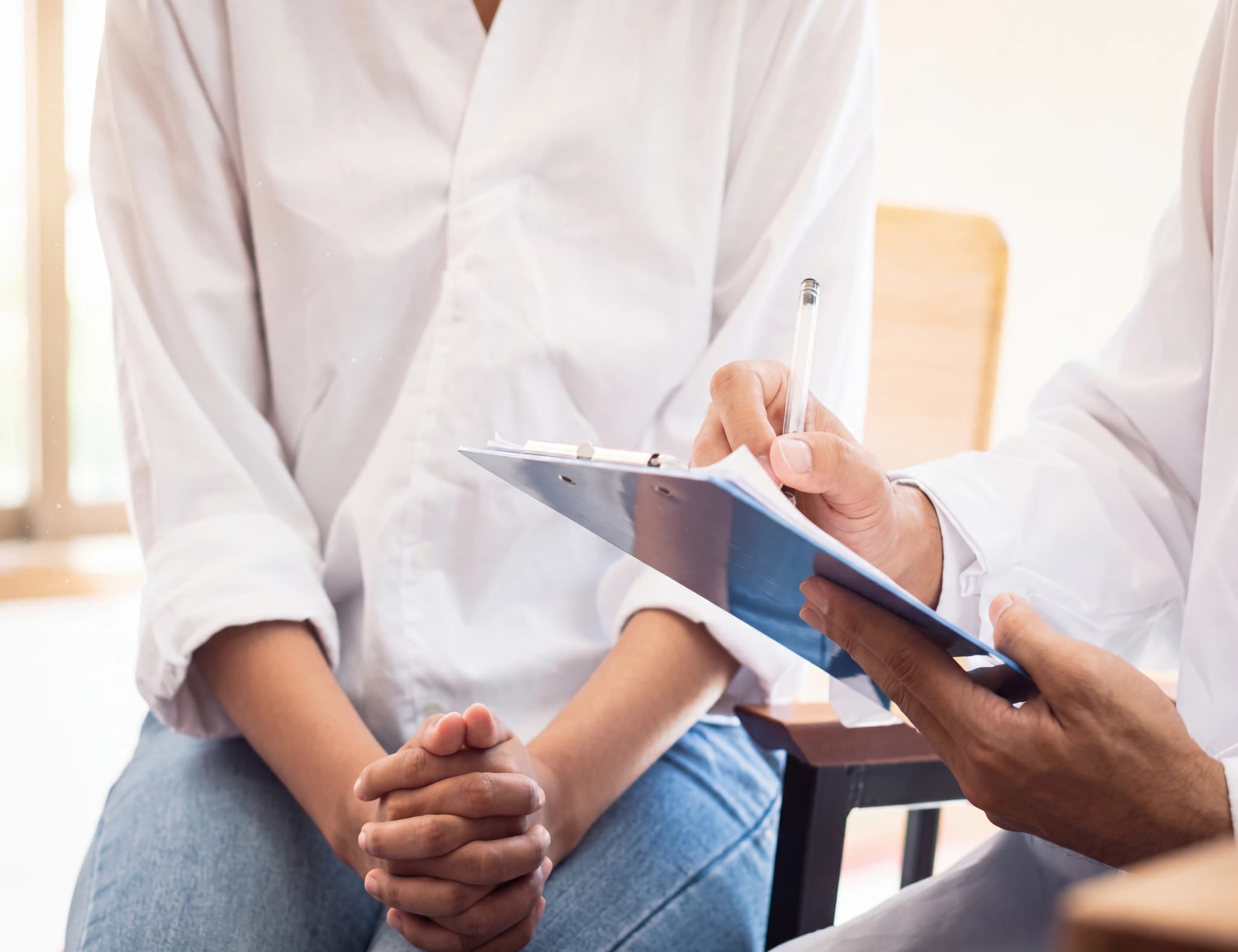 Läkare skriver anteckningar på en clipboard medan patient sitter framför.
