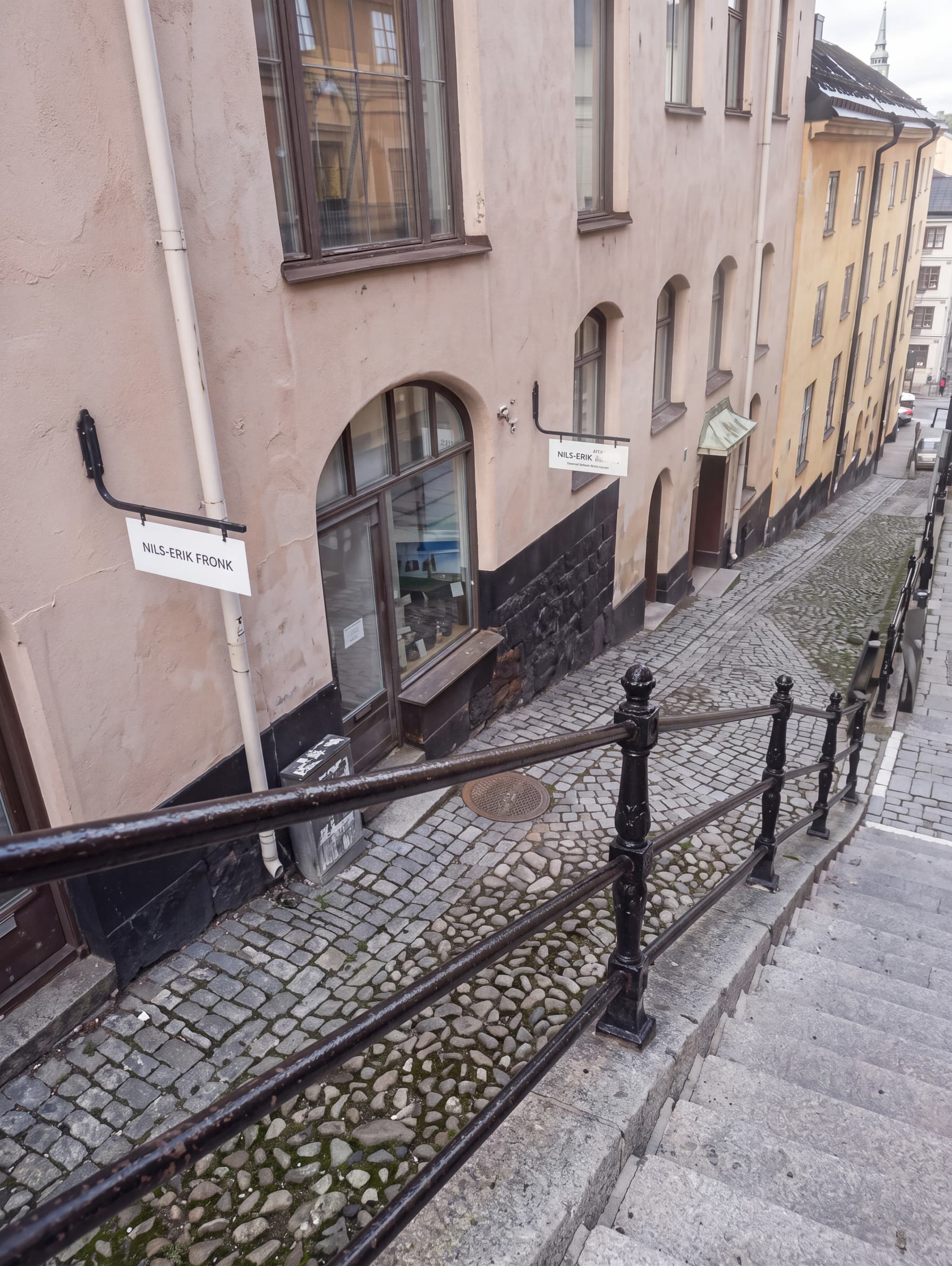 En stenlagd gata med ett räcke och byggnader längs sidorna.