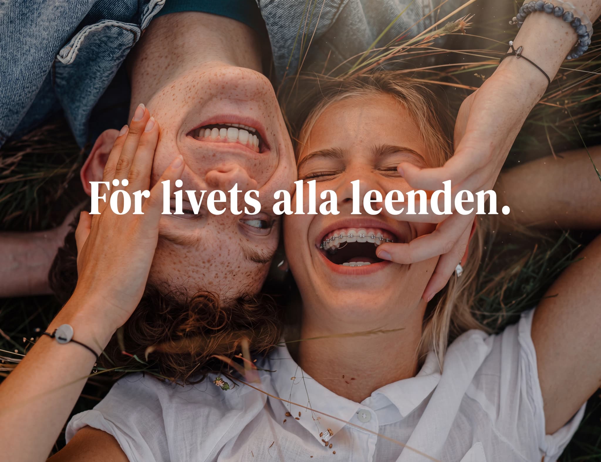Ett ungt par ligger utomhus på gräs och skrattar tillsammans, med texten "För livets alla leenden." över bilden.