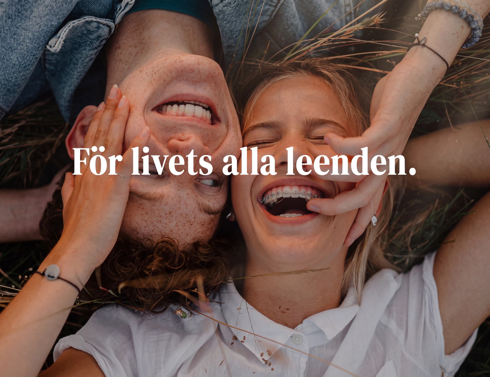 Ett ungt par ligger ner och skrattar tillsammans utomhus, med en hand som rör vid deras ansikten.