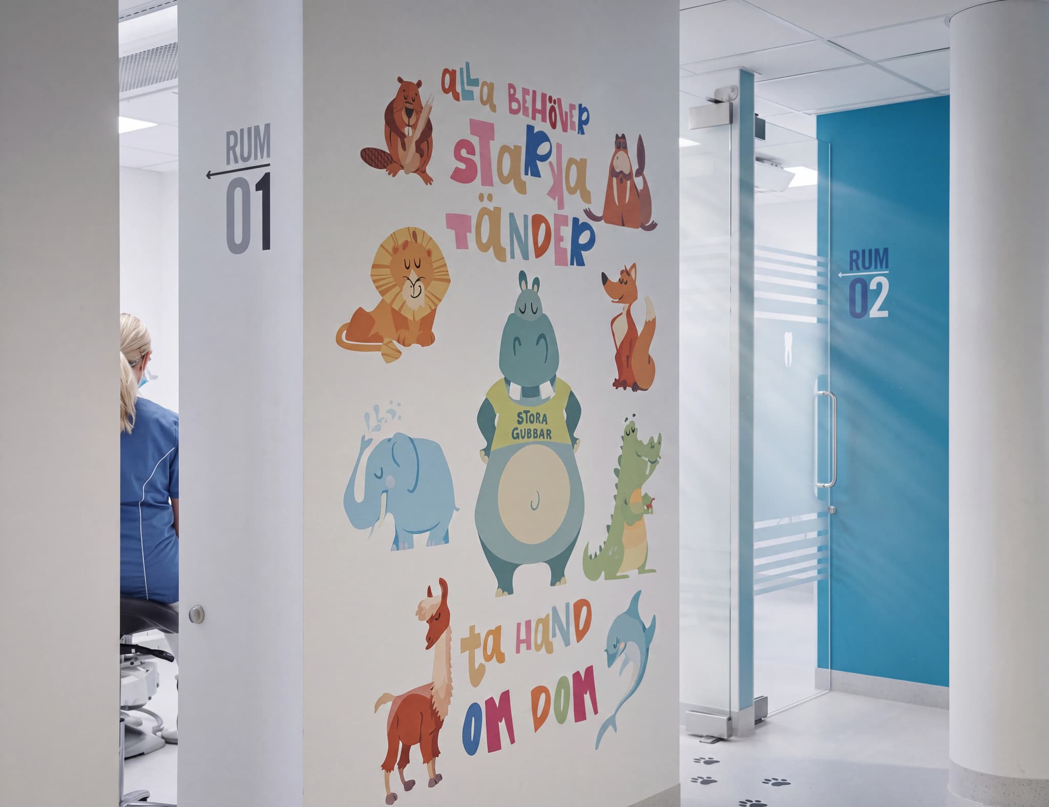 Insidan av en tandläkarmottagning med en korridor dekorerad med färgglada teckningar av djur på väggen, inklusive en flodhäst, lejon och en lama. Dörrar till rum 01 och 02 syns.