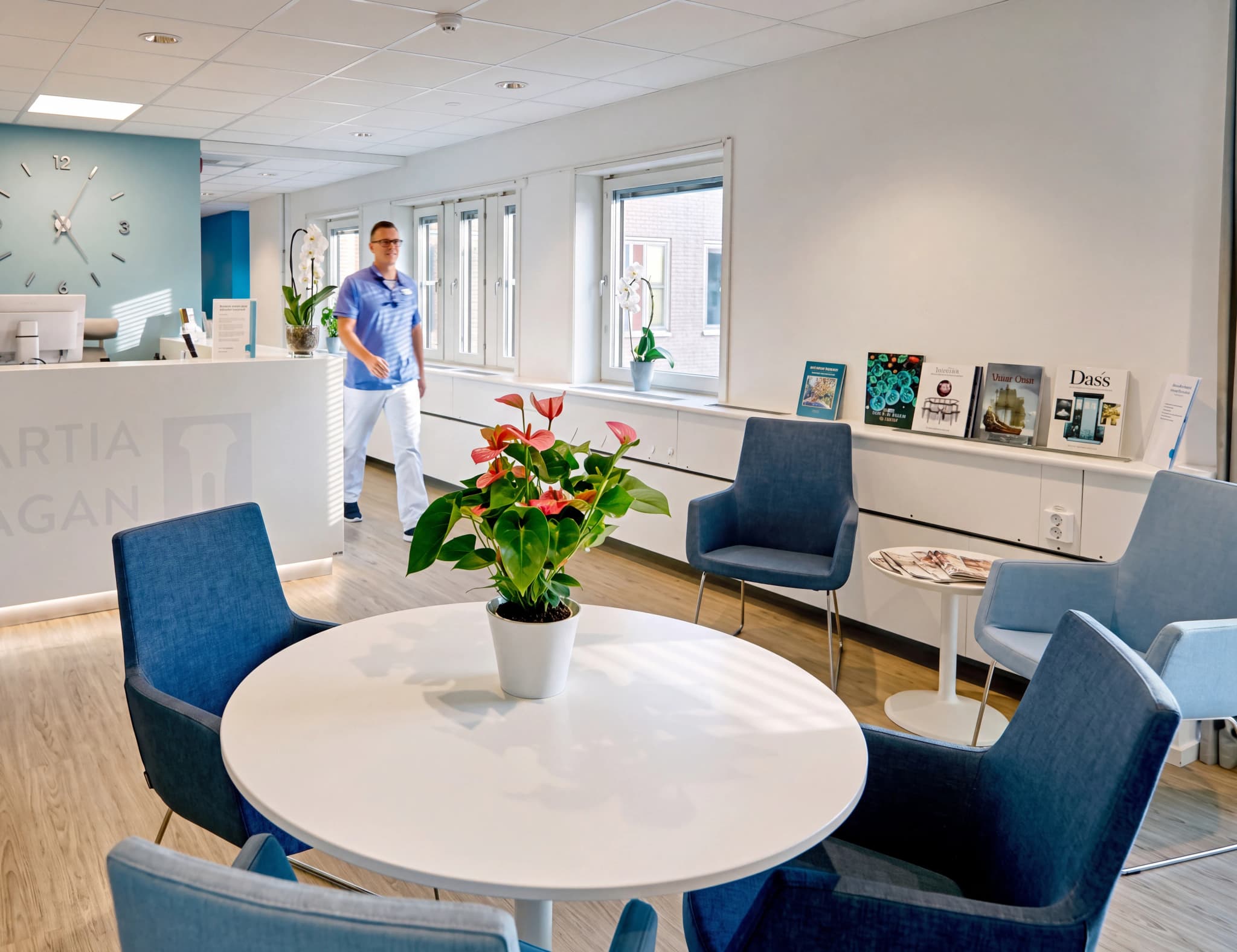 En manlig anställd i blå arbetskläder går genom en ljus och modern mottagningslokal med ett receptionsdisk och väntrum.