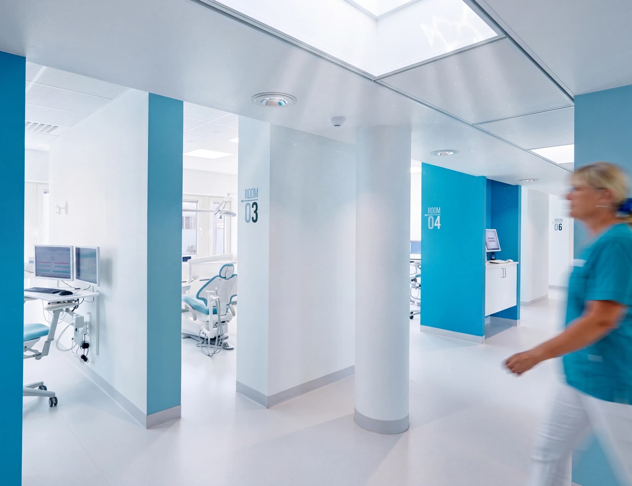 Sjuksköterska går i en ljus, modern klinikkorridor med flera rum.