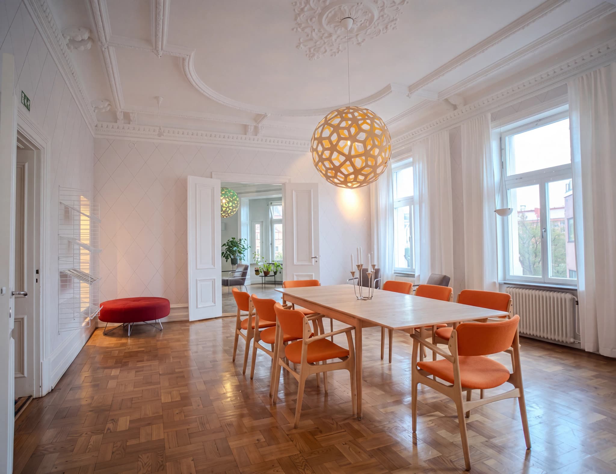 Ljus och modern matsal med parkettgolv, ett långt träbord med orange stolar och en stor bollformad lampa i taket.