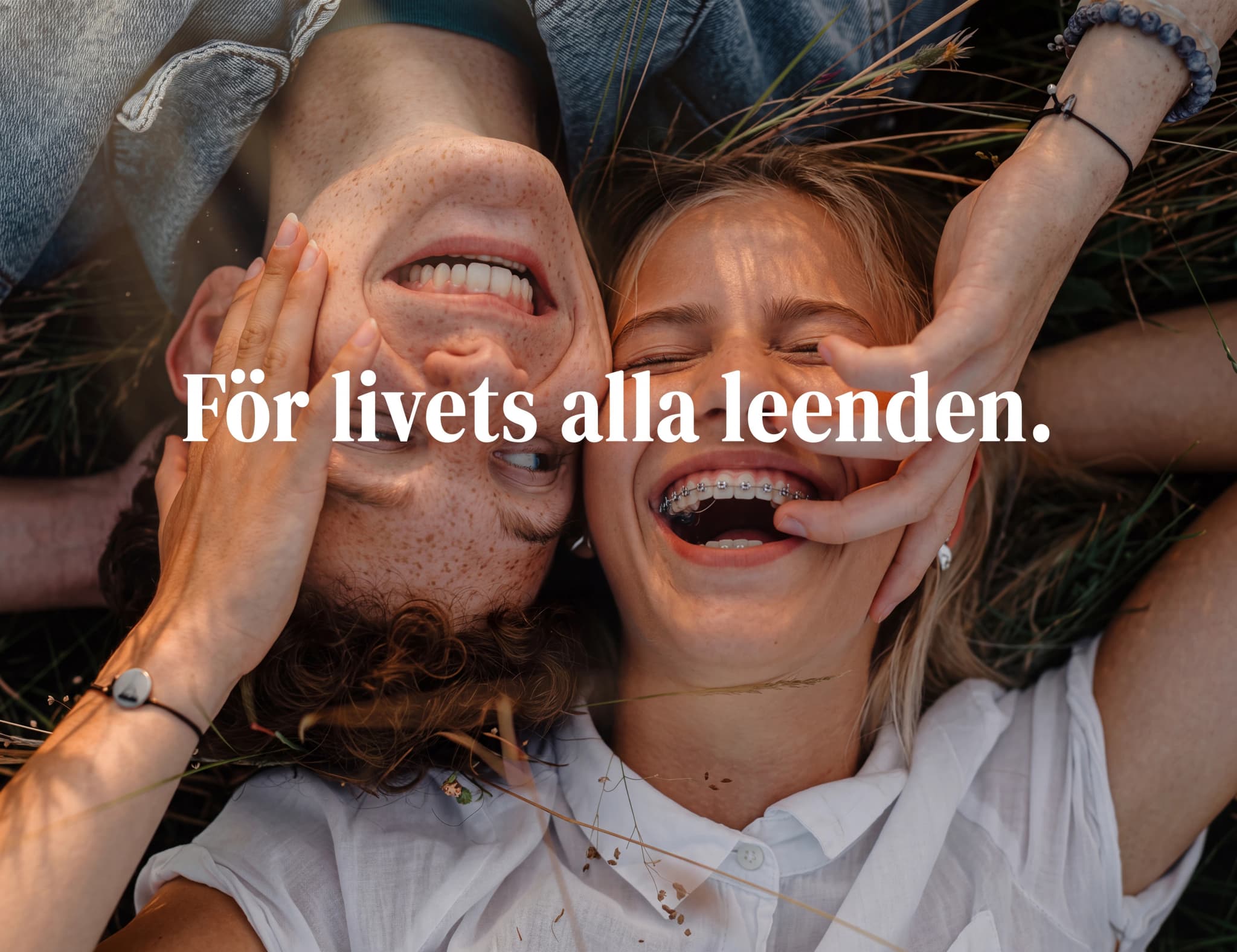 Ett ungt par ligger på rygg utomhus och skrattar, med händerna mot varandras ansikten.