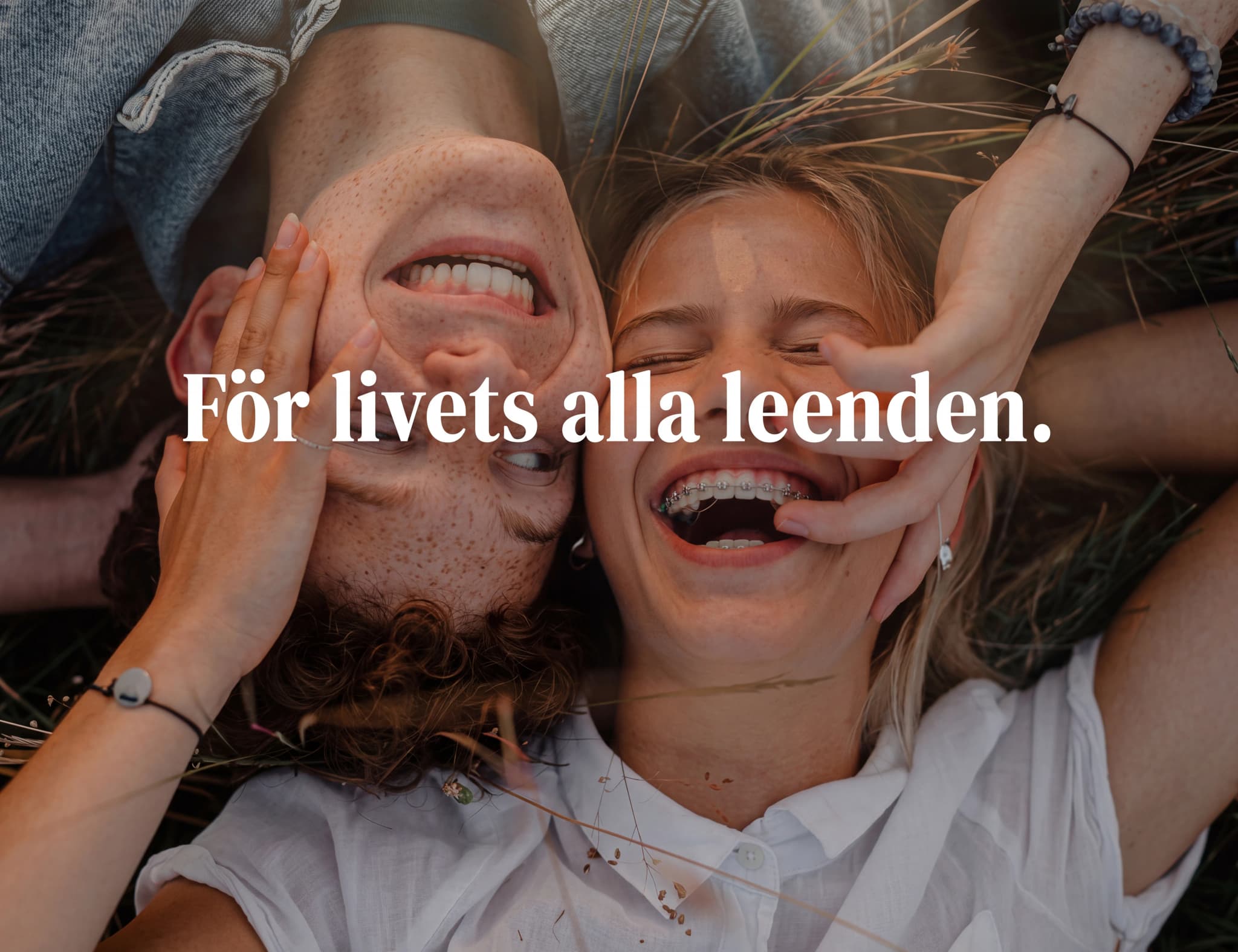 Ett ungt par ligger på marken och skrattar tillsammans utomhus.