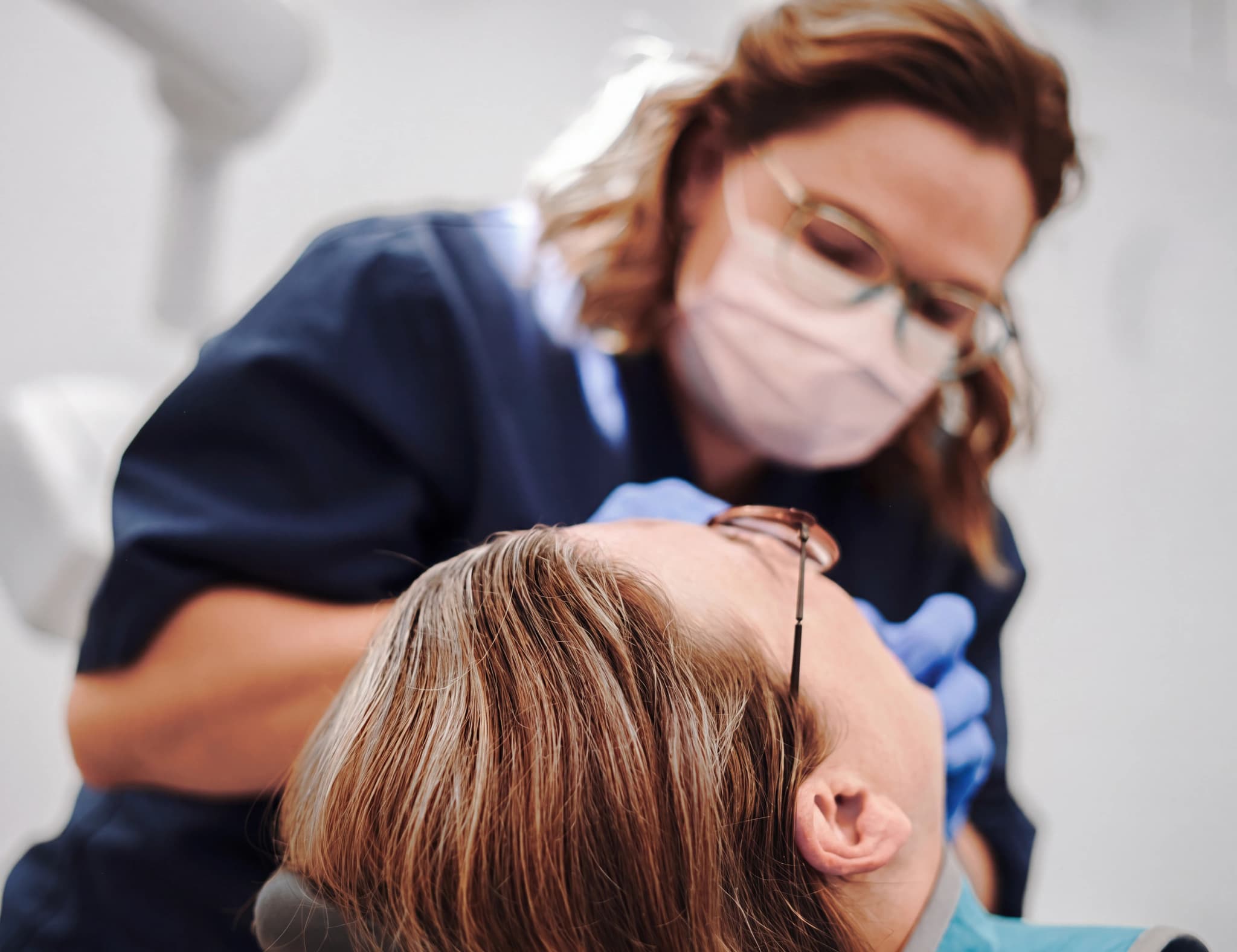 Tandläkare med skyddsmask undersöker en patients tänder med ett instrument på en klinik.