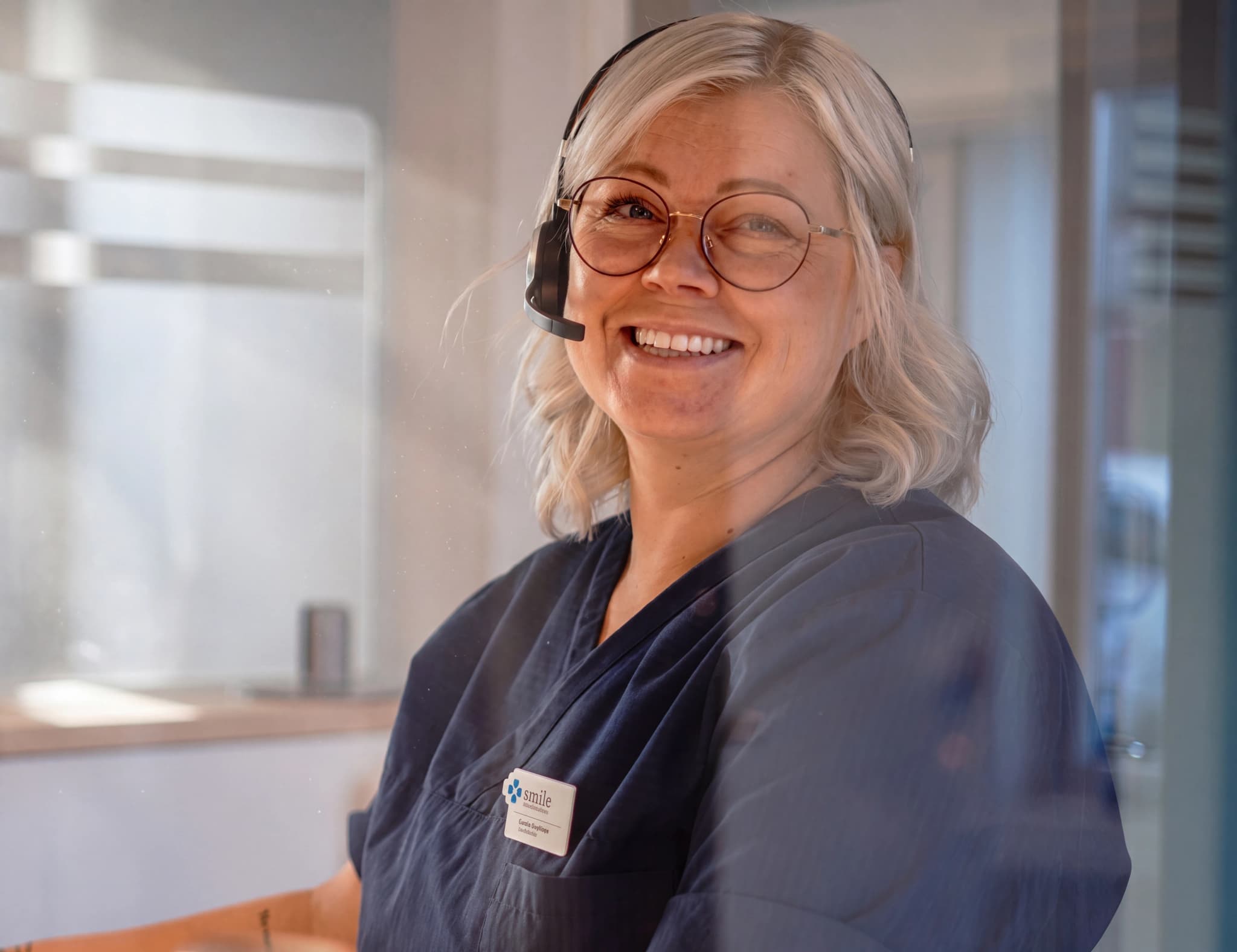 En leende receptionist med headset på sig sitter vid ett skrivbord och tittar framåt.
