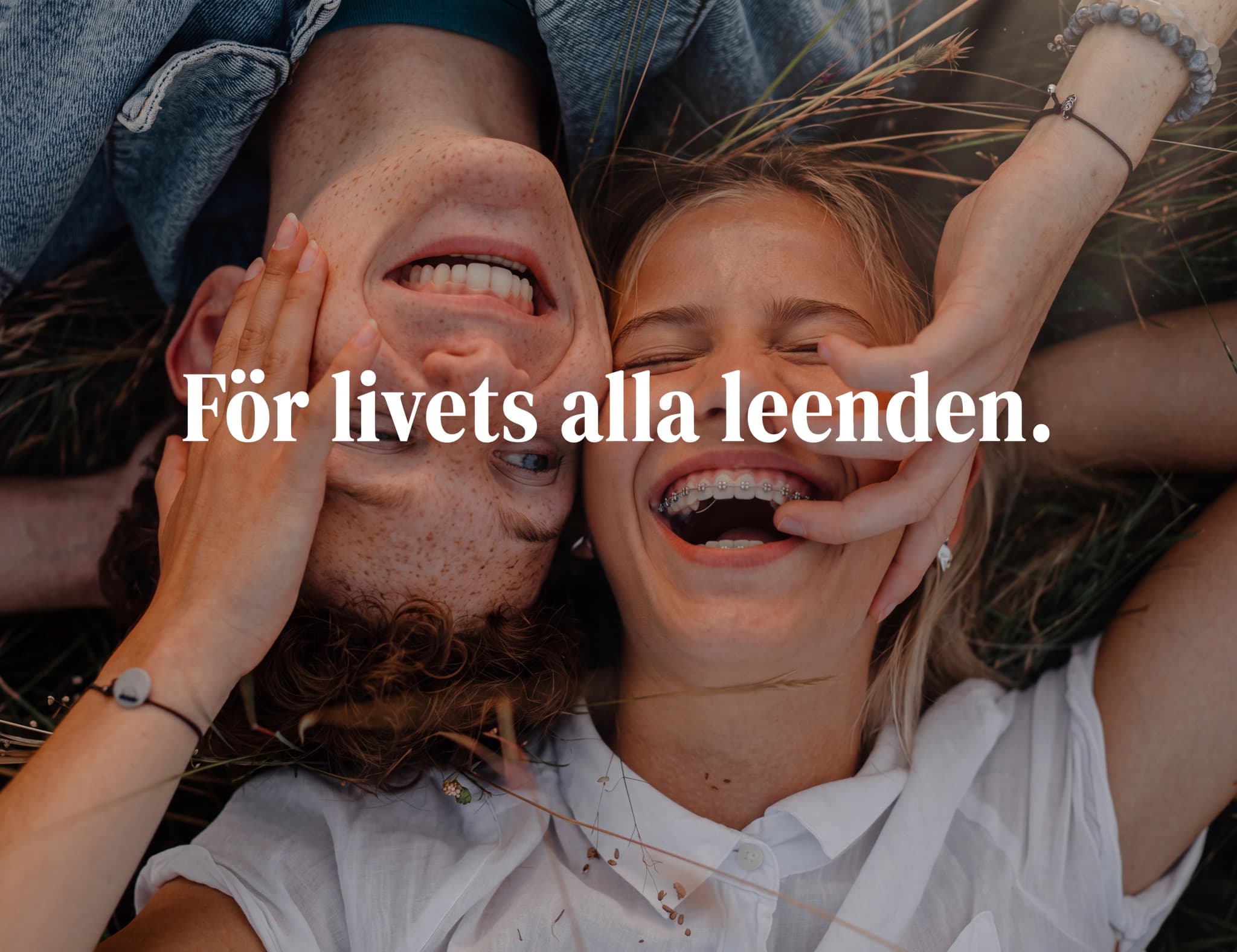 Ungt par som ligger ner på gräs och skrattar, med texten "För livets alla leenden."