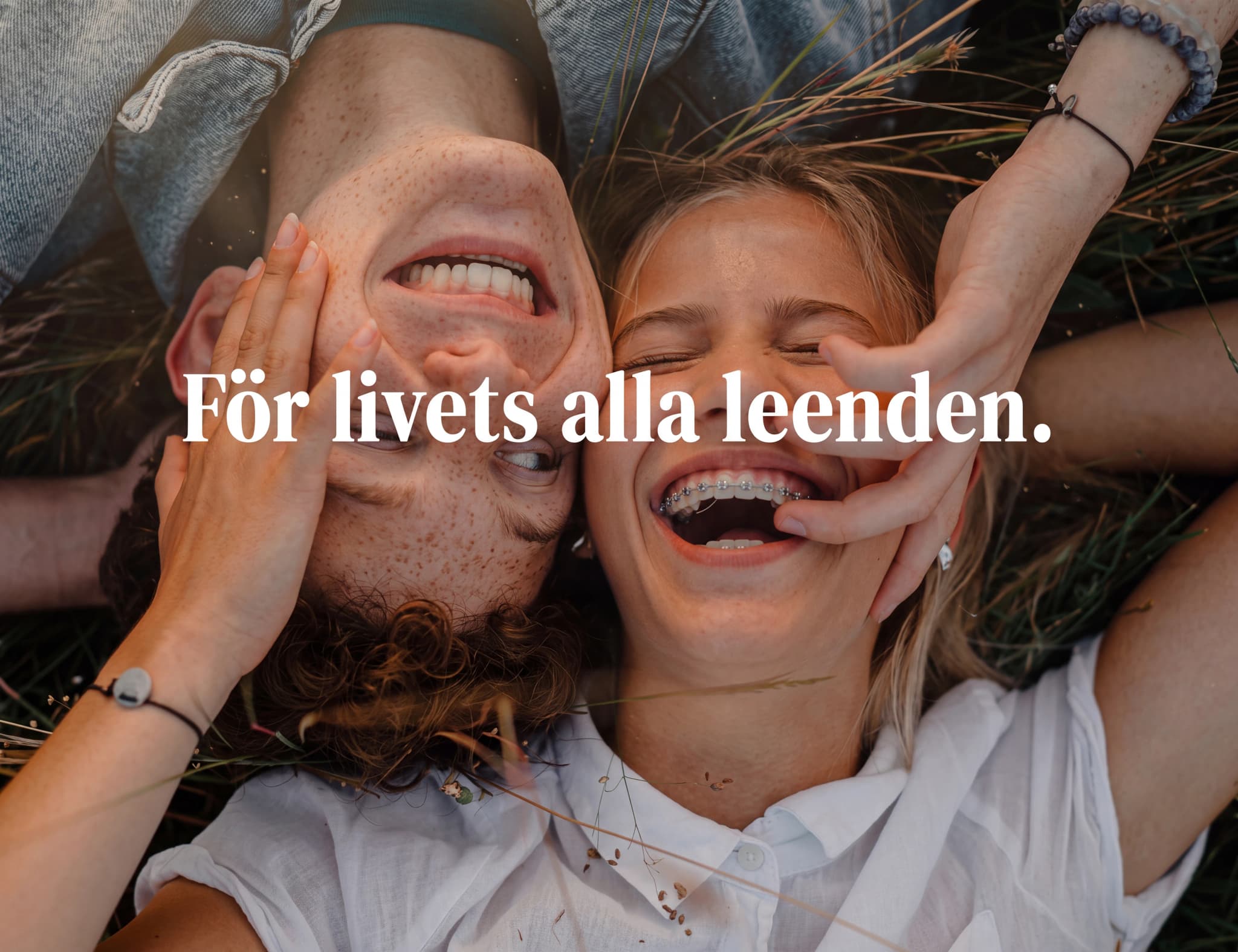 Ungt par som skrattar och ligger ner utomhus med texten "För livets alla leenden."