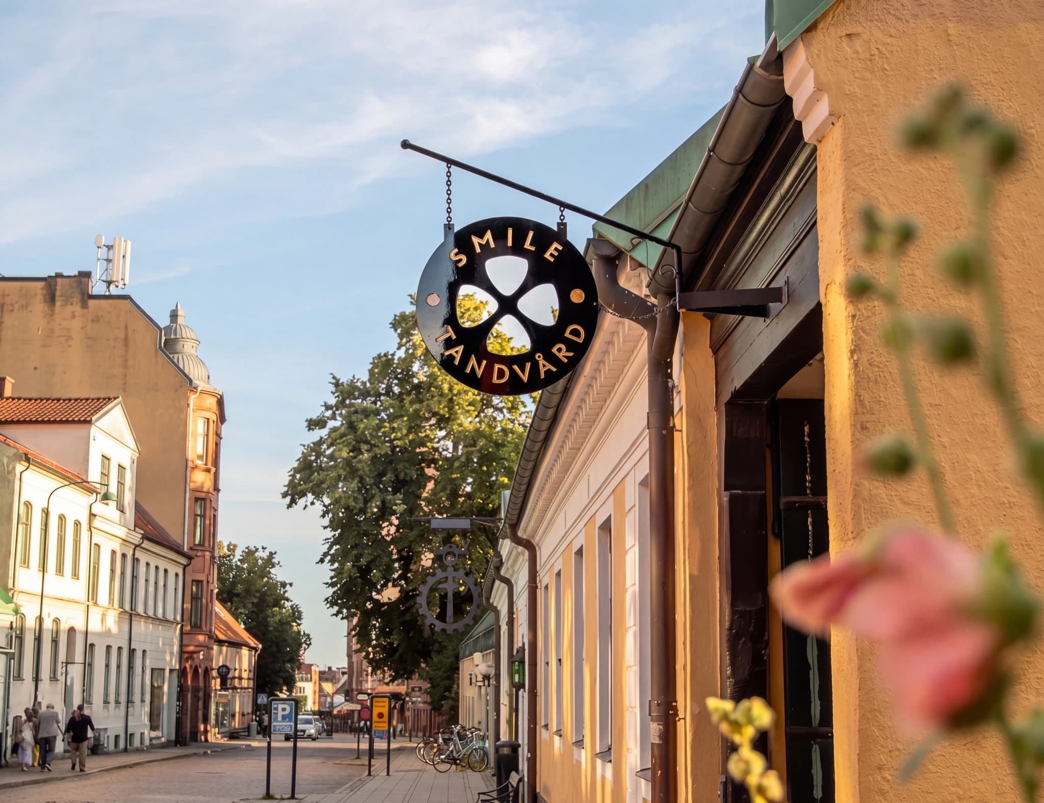 Rund skylt med texten 'SMILE Tandvård' som hänger utanför en byggnad i en stadsgata.