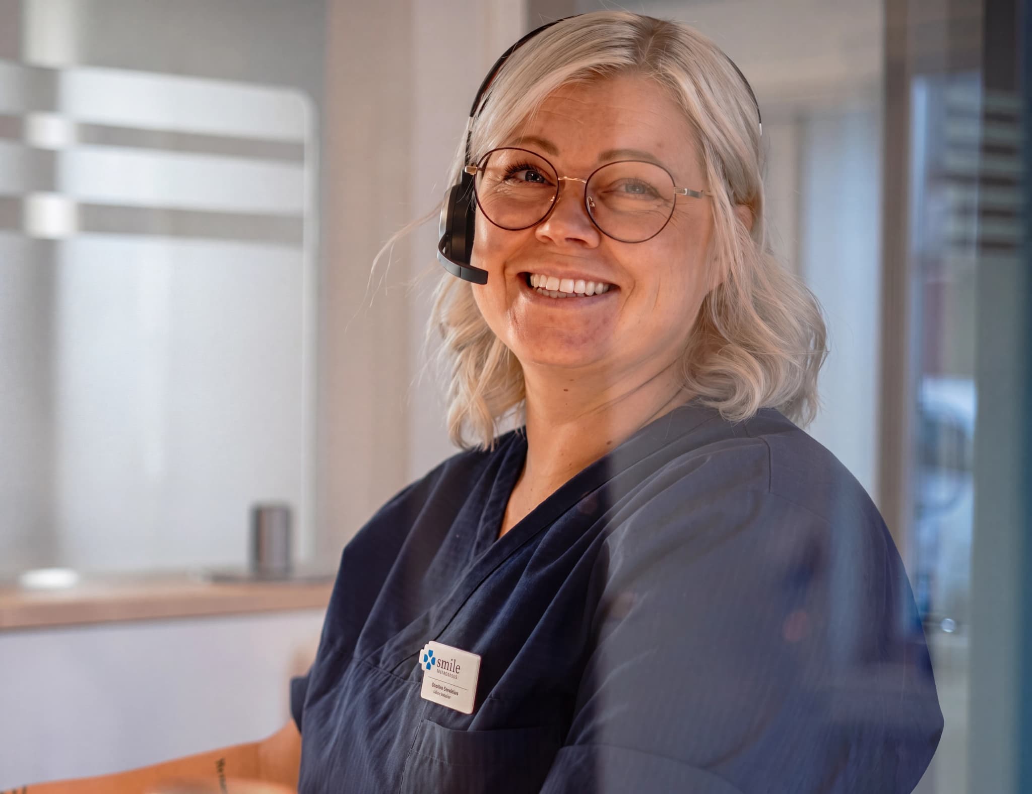 En leende kvinna i receptionen med headset och glasögon.