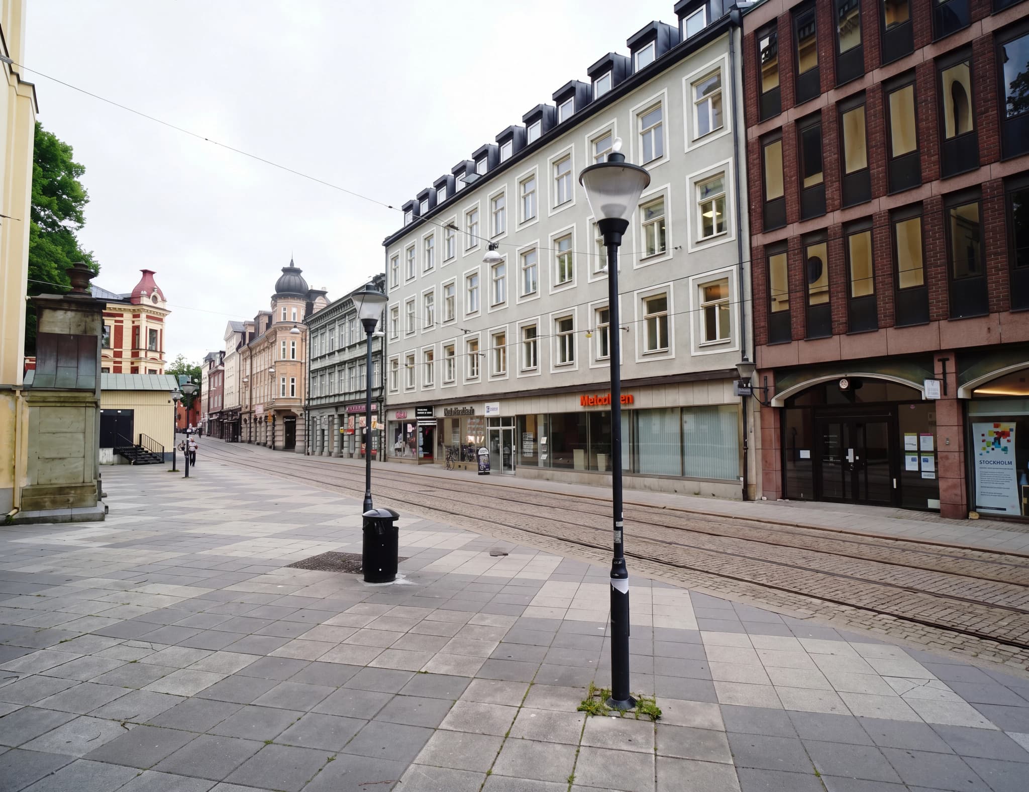 En tom gata med spårvagnsräls och butiksfasader längs en trottoar.