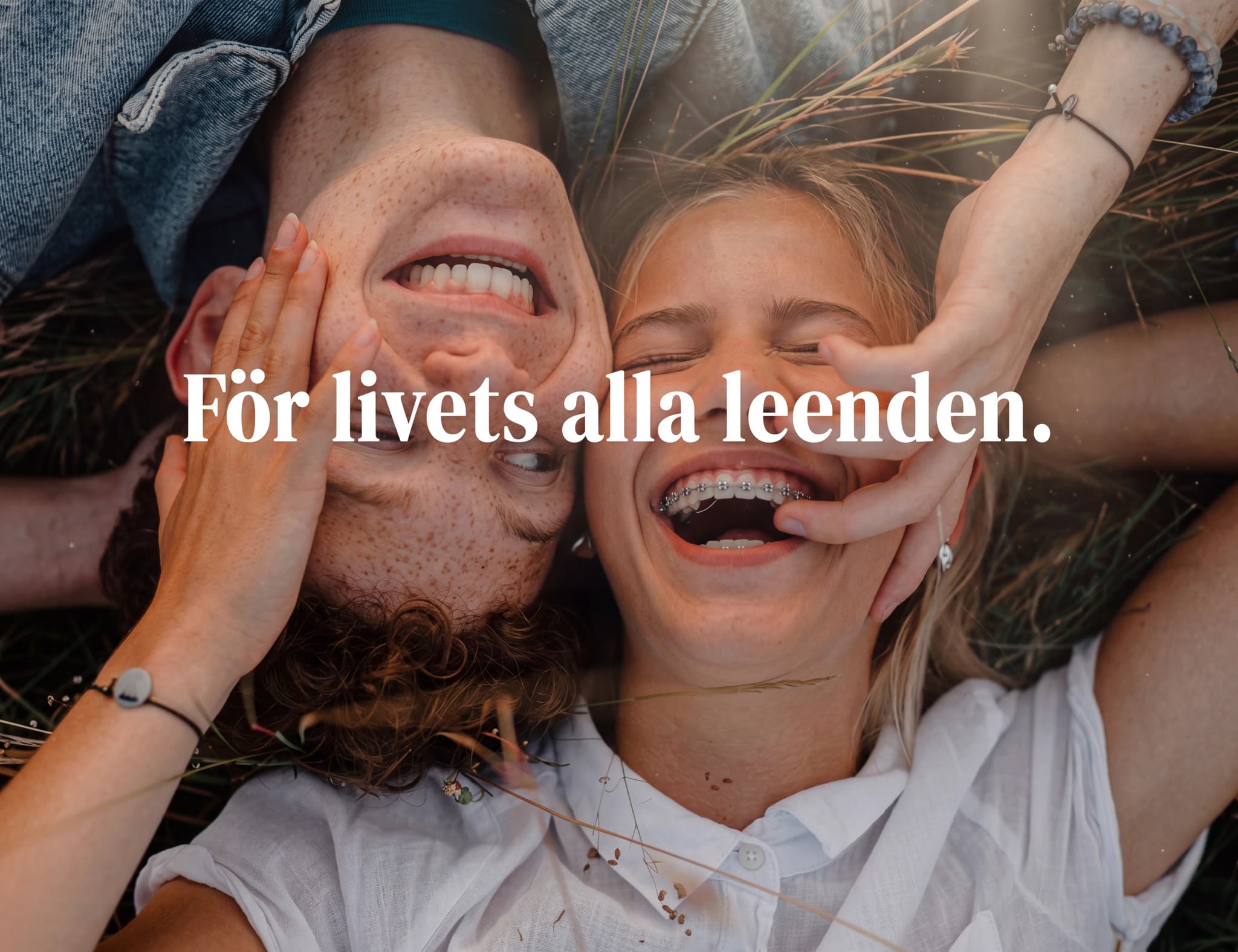 Ett ungt par ligger på rygg och skrattar, med en hand som rör vid deras ansikten och texten "För livets alla leenden." över bilden.