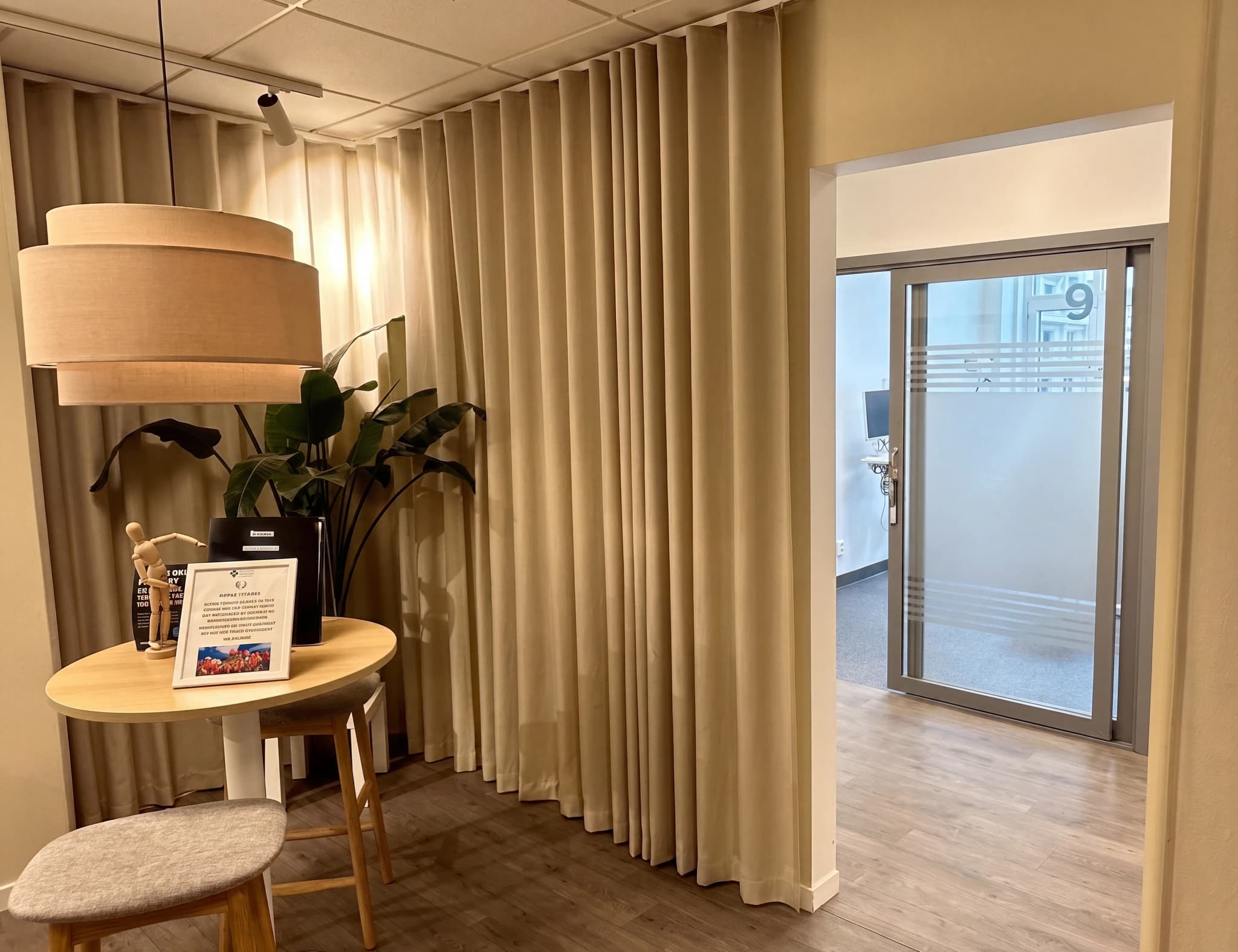 Receptionområde med ett runt bord, en växt, en lampa och en skjutdörr i bakgrunden.