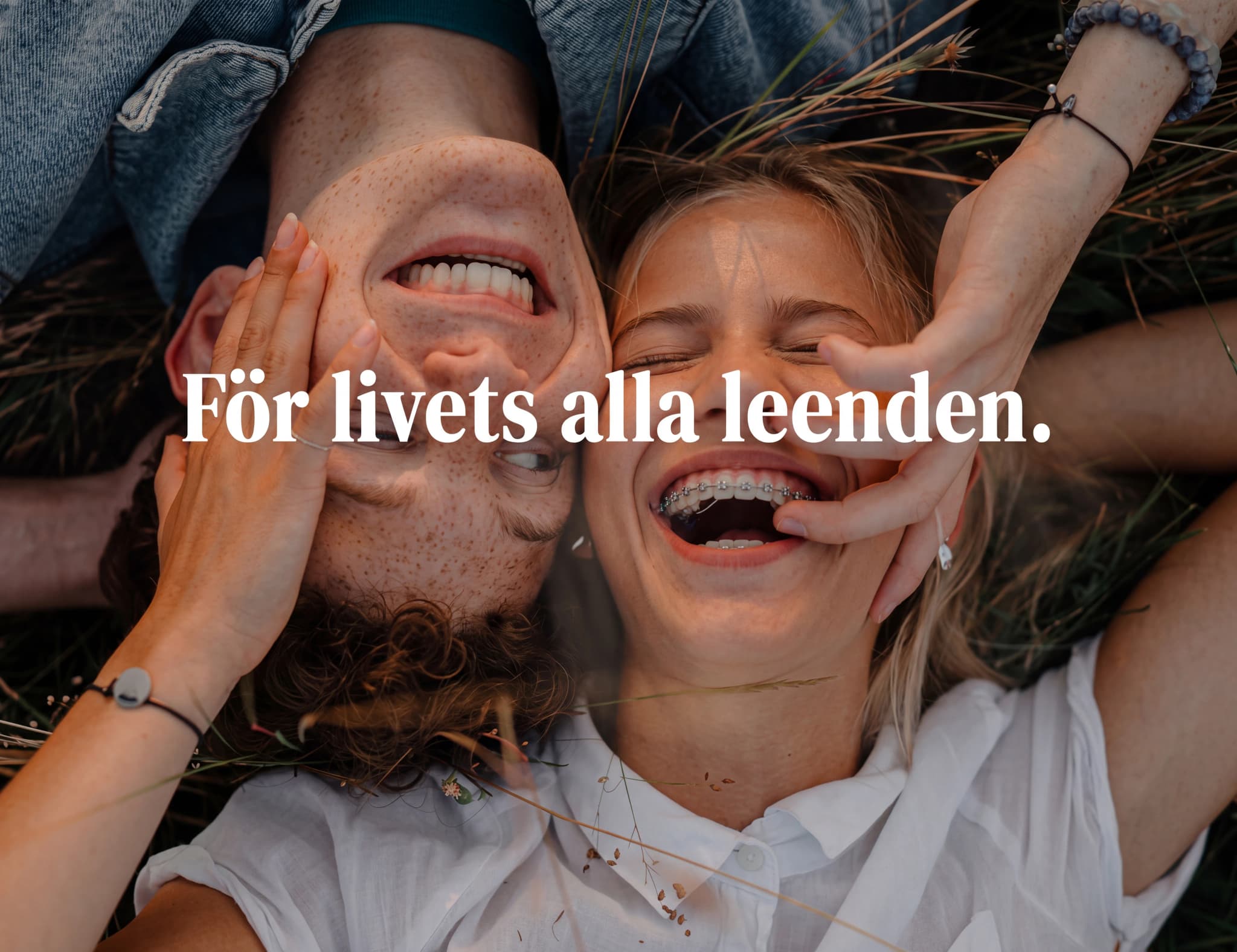 Ungt par ligger på rygg i gräset och skrattar tillsammans, med grässtrån runt omkring dem. Texten "För livets alla leenden." är överlagd.