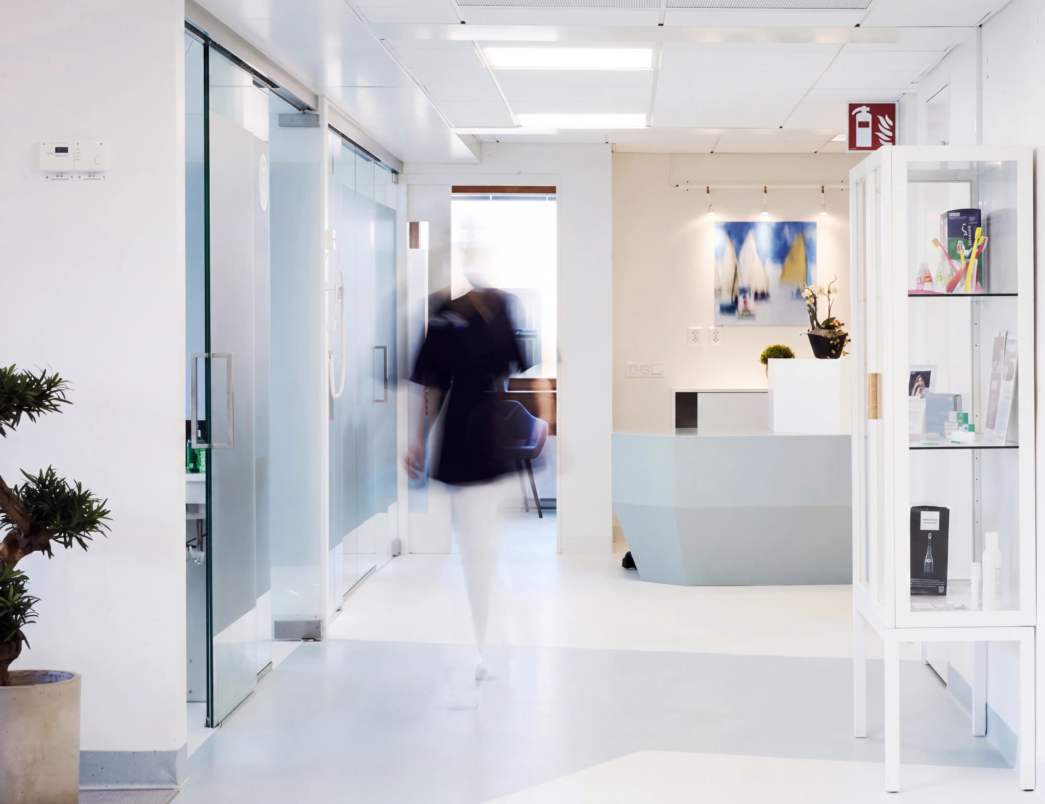 En person i rörelse går genom en ljus klinikkorridor mot en reception med en receptionsdisk och konst på väggen.