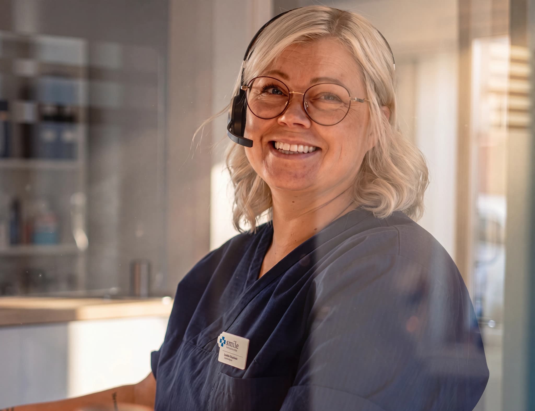 En kvinna med headset och glasögon ler mot kameran vid en reception.