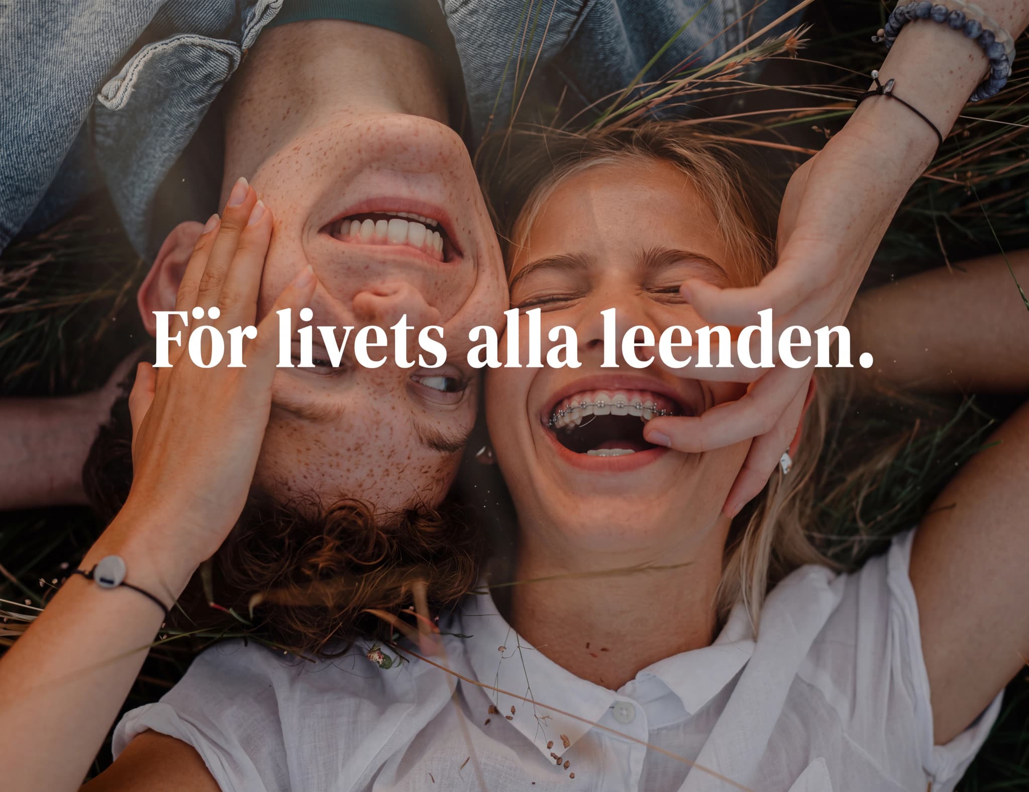 Ett ungt par ligger utomhus och skrattar, med texten "För livets alla leenden." över bilden.
