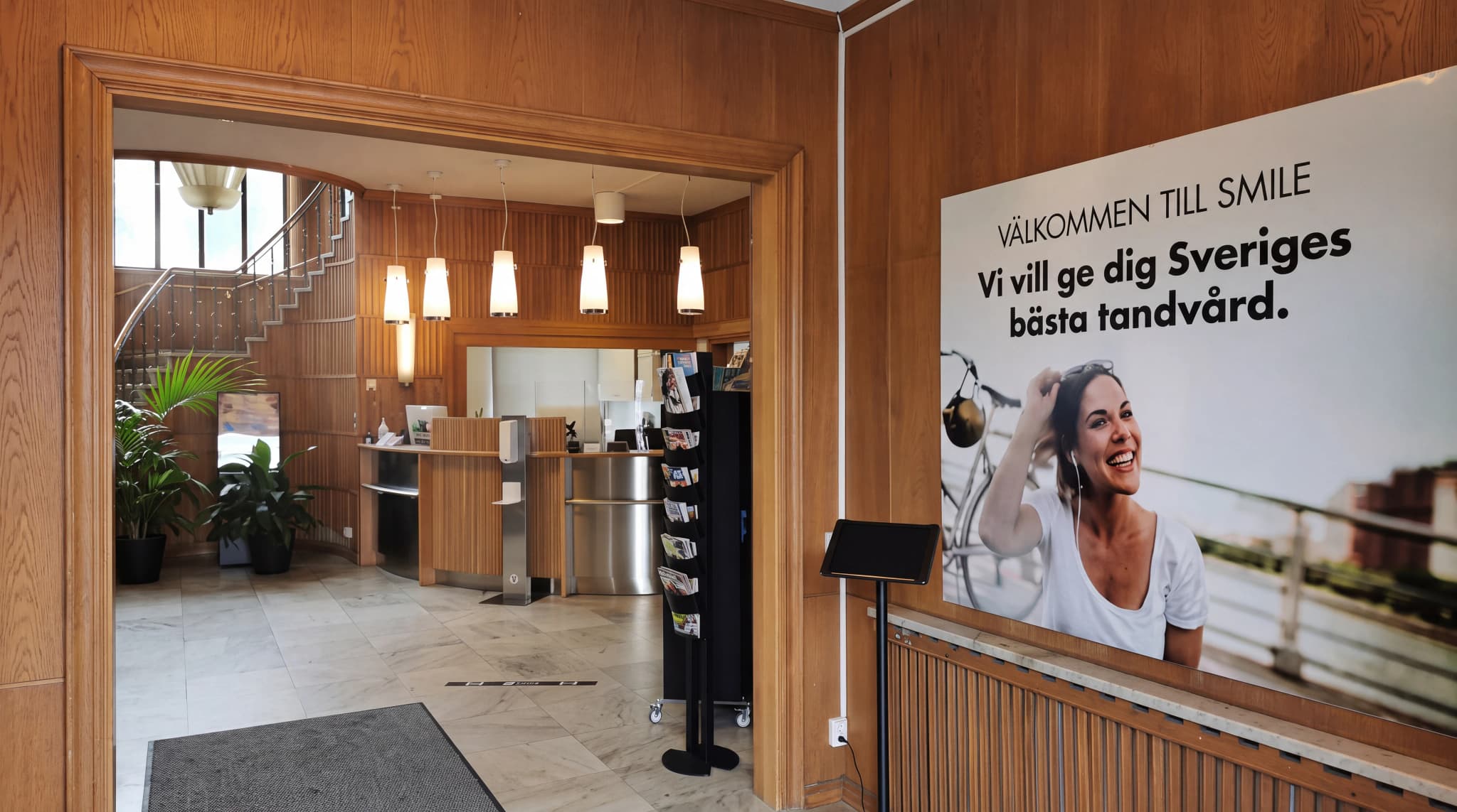 Entréhallen på en klinik med reception, trappa och en stor affisch med texten 'Välkommen till Smile' och en glad kvinna.