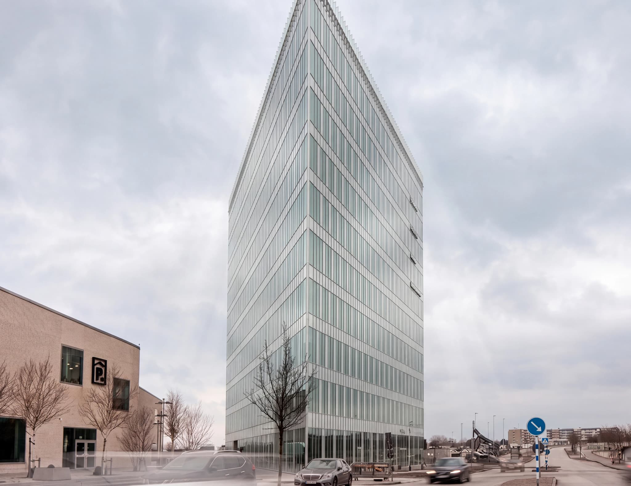 Modern glasbyggnad med glasfasad och ett molnigt himmel.