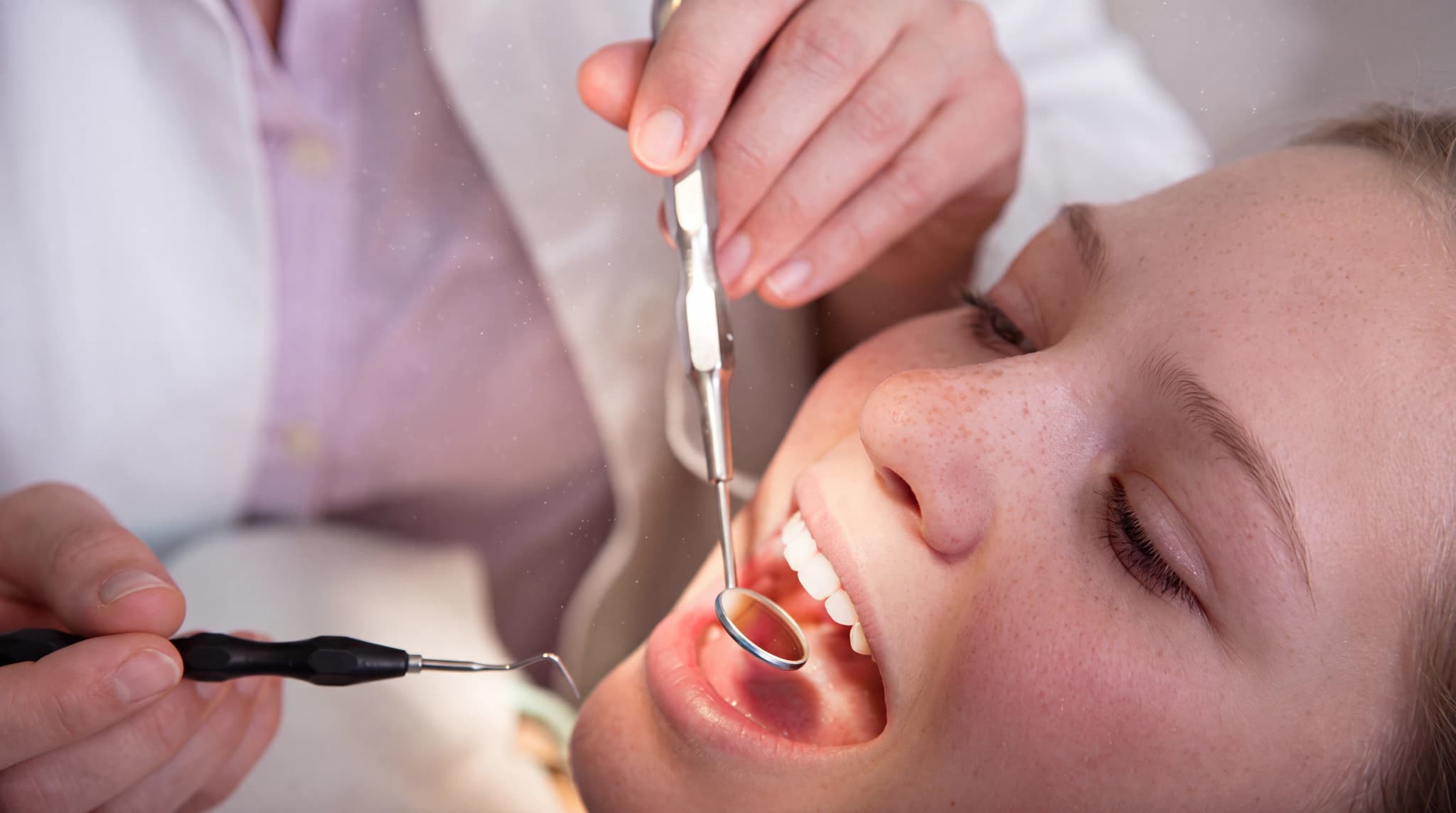 Tandläkare undersöker patientens mun med dentalverktyg som en spegel och en sond.